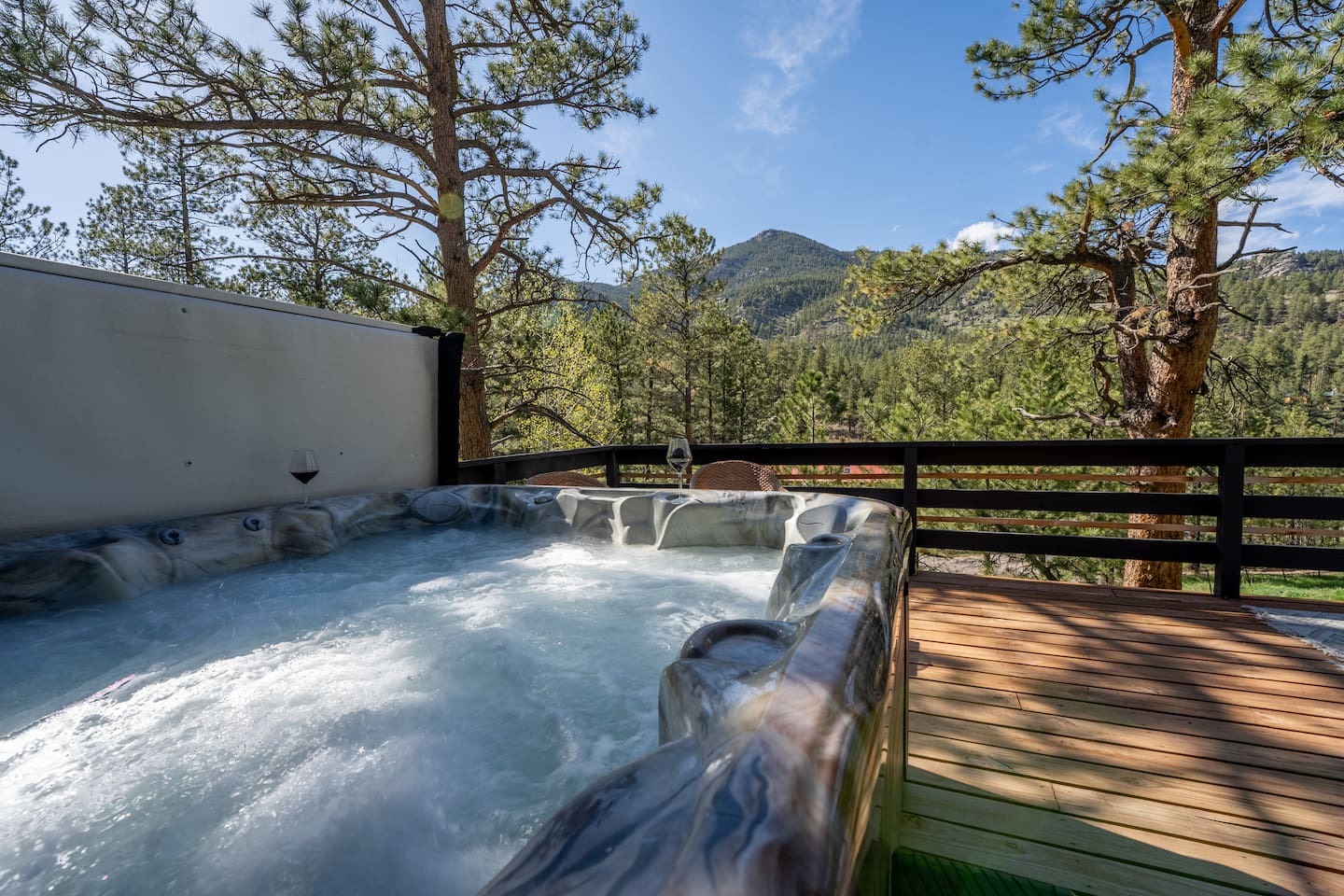 Hot tub on the deck with pines and mountains in the distance under a blue sky