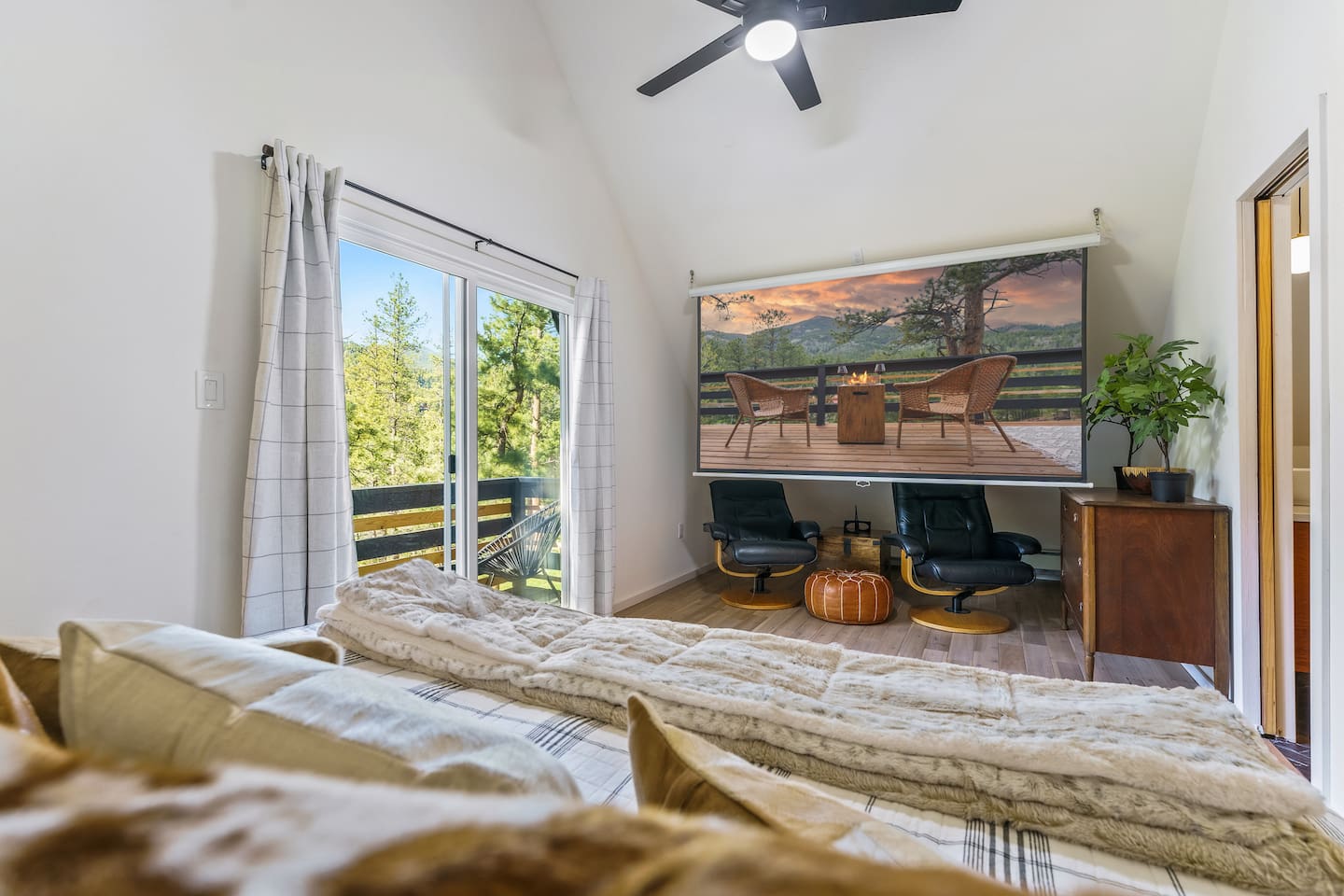 Primary bedroom with a king bed facing a projector screen and sliding doors to a deck