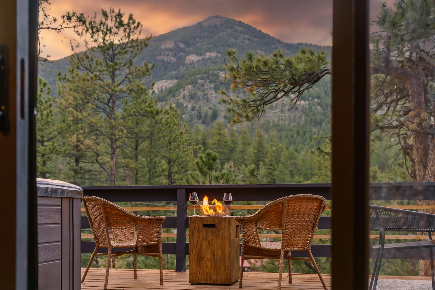 Fire table and two wicker chairs on the covered deck, framing a mountain peak