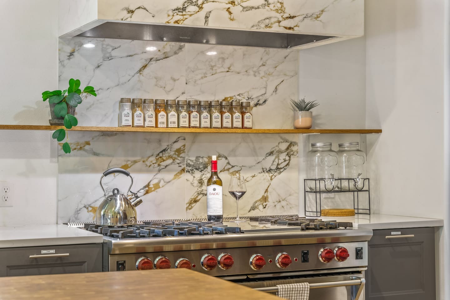 Wolf range with red knobs under a marble backsplash and an open spice shelf