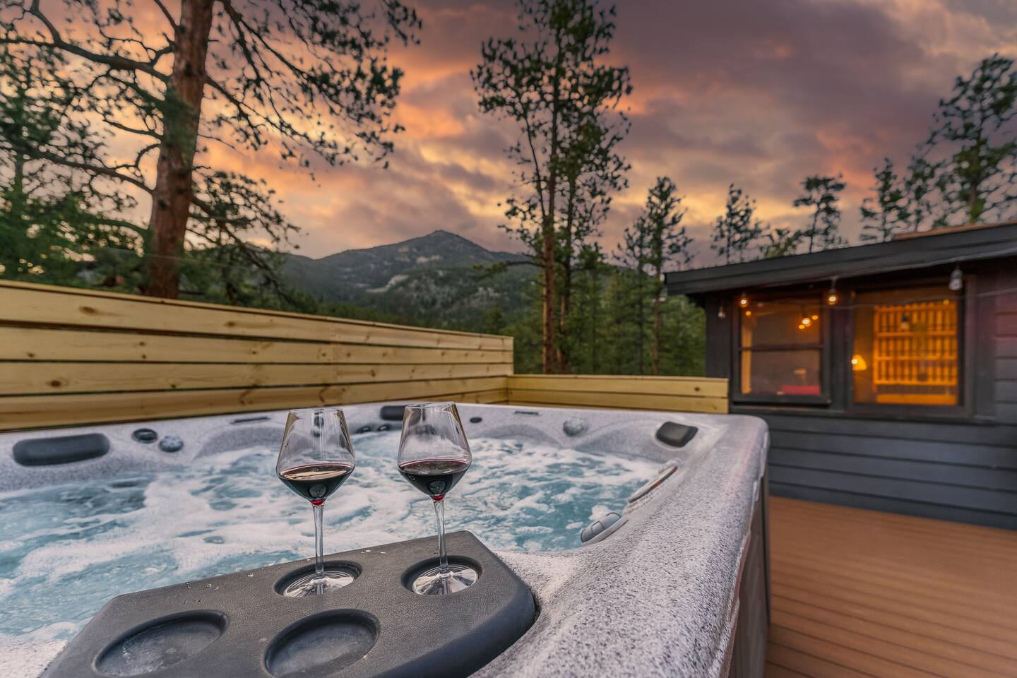 Hot tub on the deck with two glasses of wine and a mountain at sunset