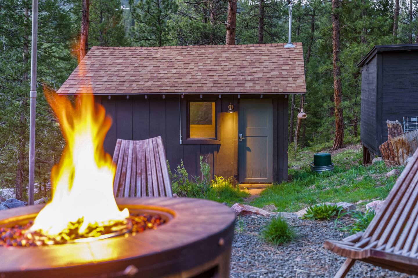 Fire pit blazing at dusk with sling chairs and the Writer’s Nook behind