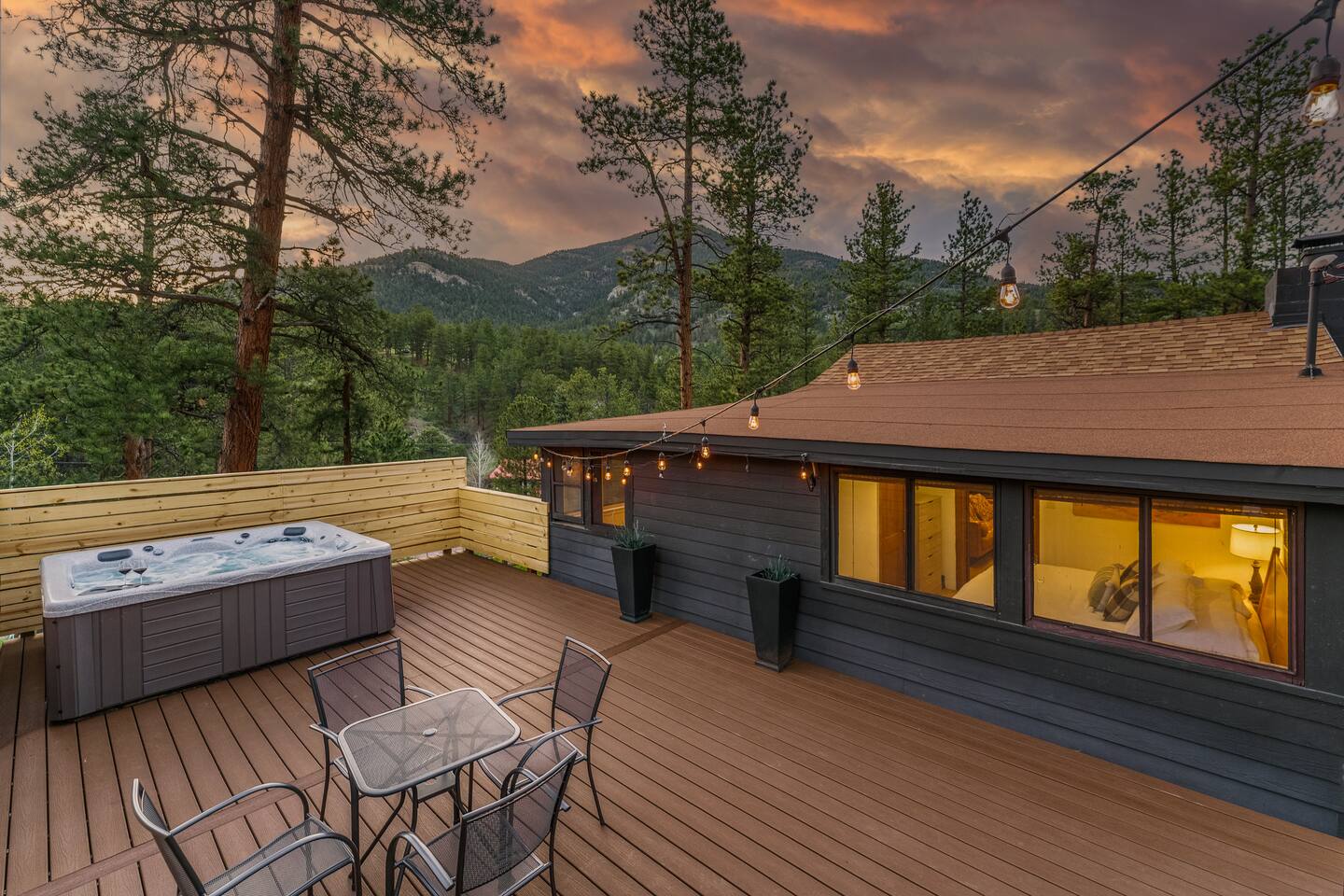 New deck at dusk with a hot tub, a bistro table and the lit-up cabin