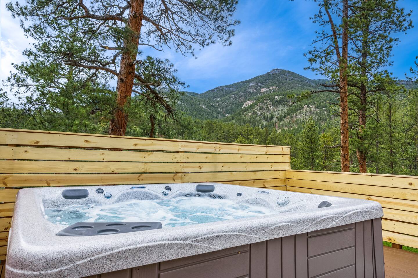 Hot tub on the deck facing a forested mountain on a sunny day