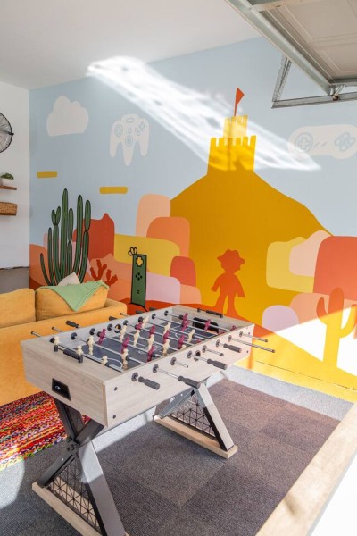 Fun Garage Game Room! ⚽ Get ready to play in this unique space featuring a vibrant, custom desert castle mural and foosball table. A bright orange sofa provides a comfy spot to watch or wait your turn. Unique and playful fun for all ages!