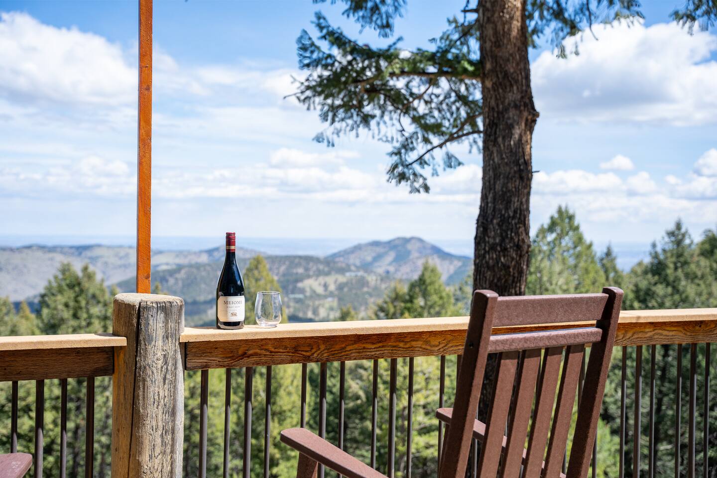 A bottle of wine on the deck rail with a view over the valley