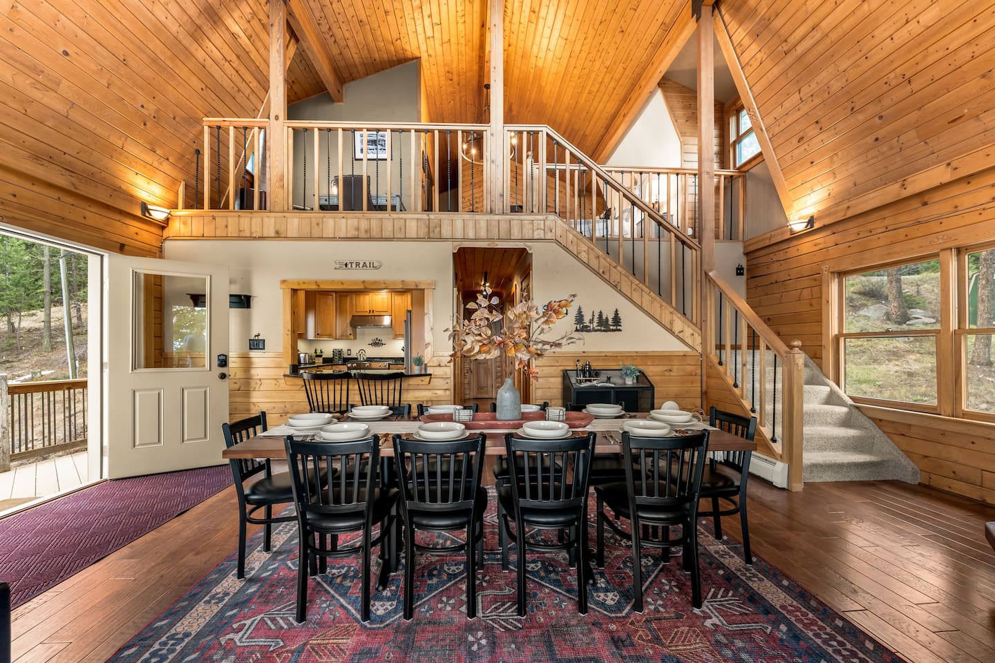 Timber dining hall with a long table under a chandelier and an open loft above