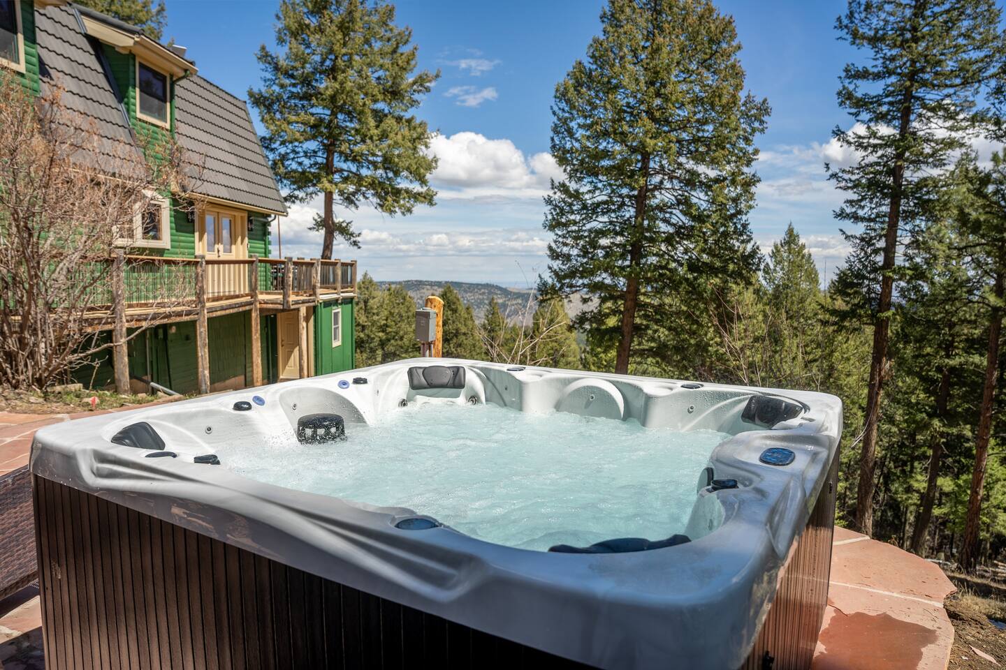 Hot tub on a stone patio with pines and a mountain view on a sunny day