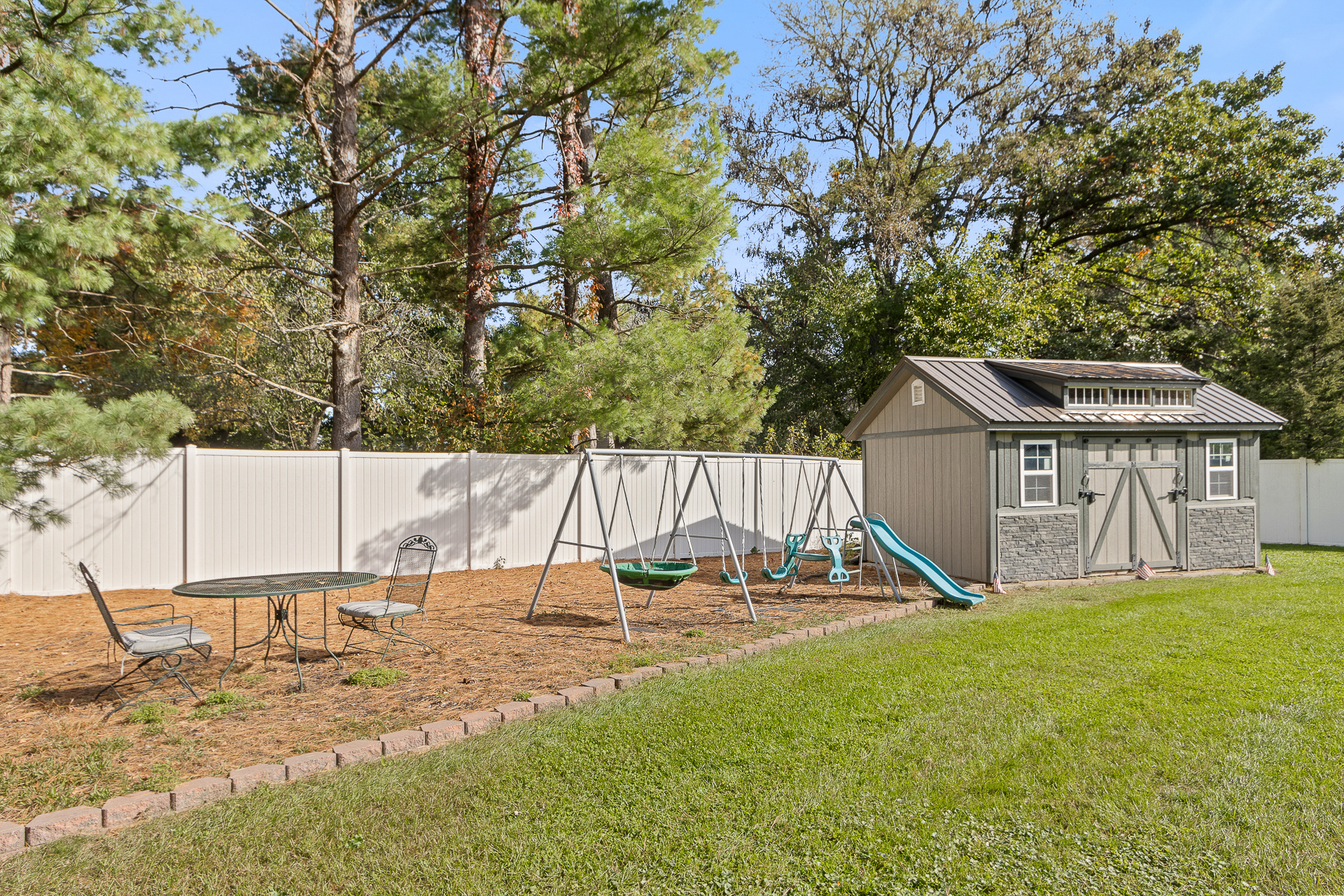 Family-friendly fenced yard with playset, lawn, and peaceful tree-lined setting