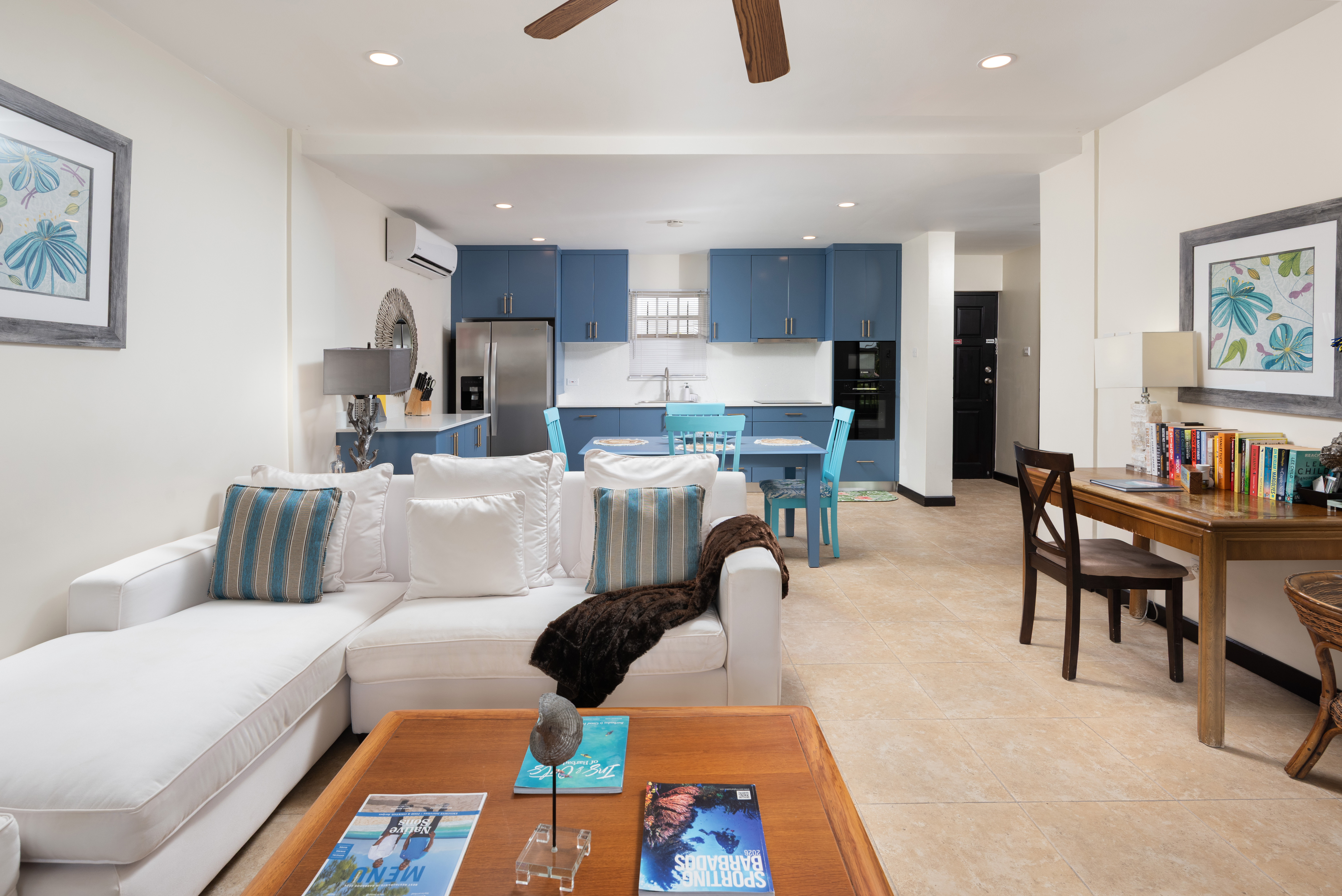 Bright open-concept living with blue kitchen, dining nook, and workspace