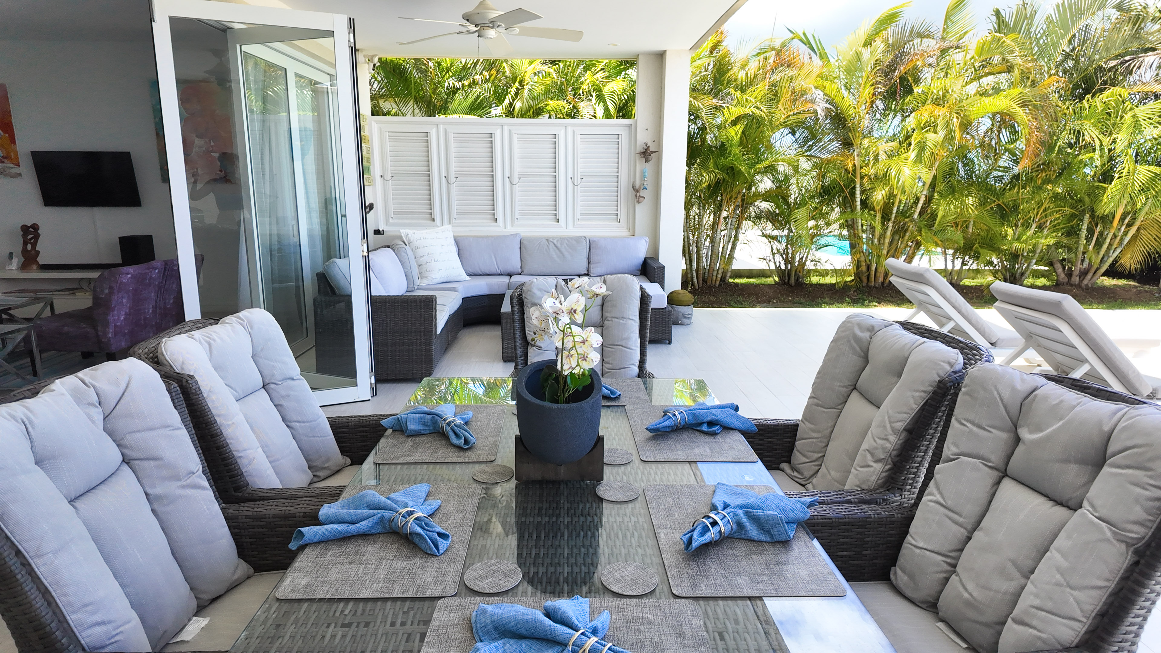 Covered tropical patio with outdoor dining, lounge seating, and poolside views