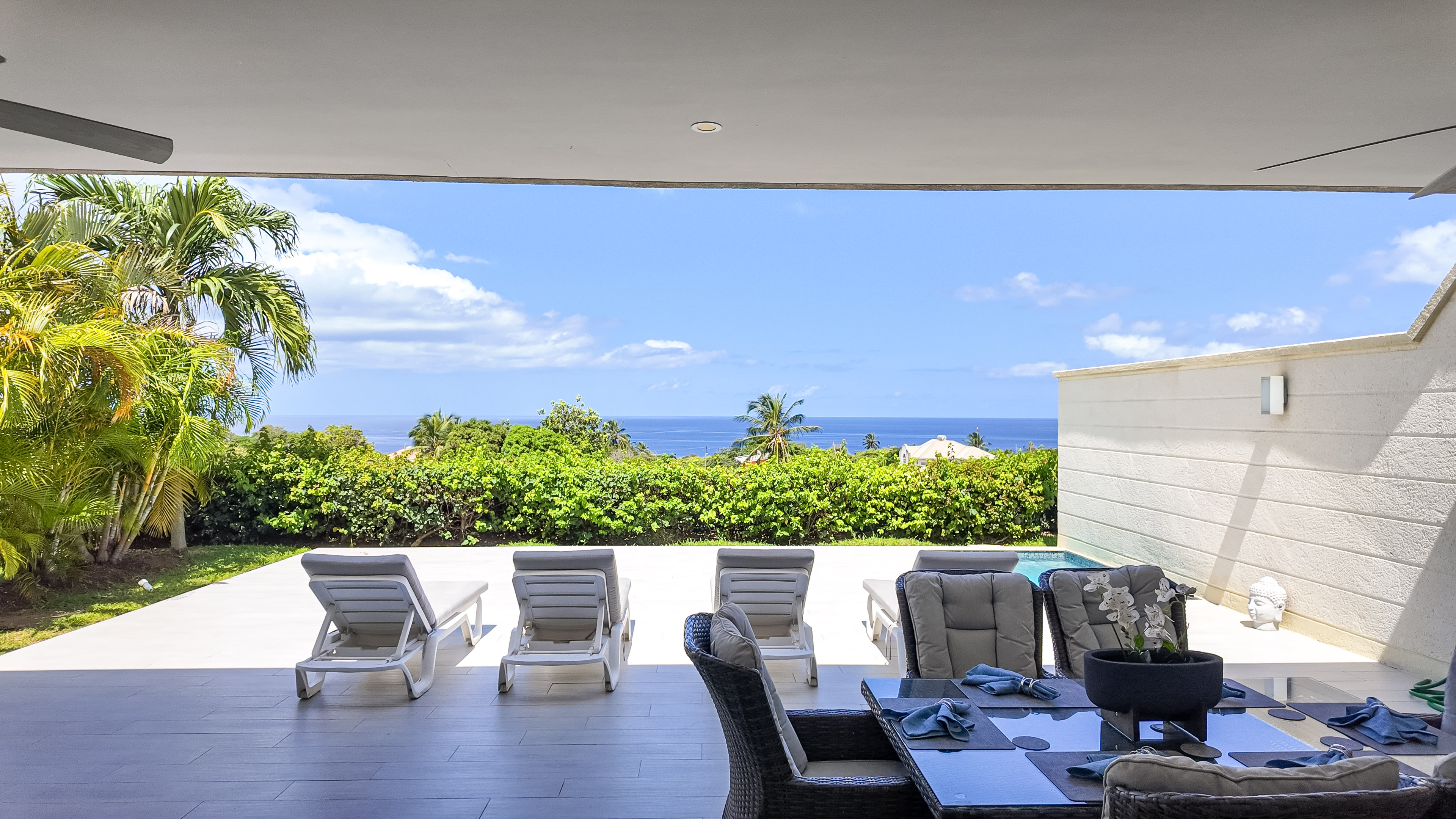 Covered ocean-view patio with loungers, dining space, and tropical privacy