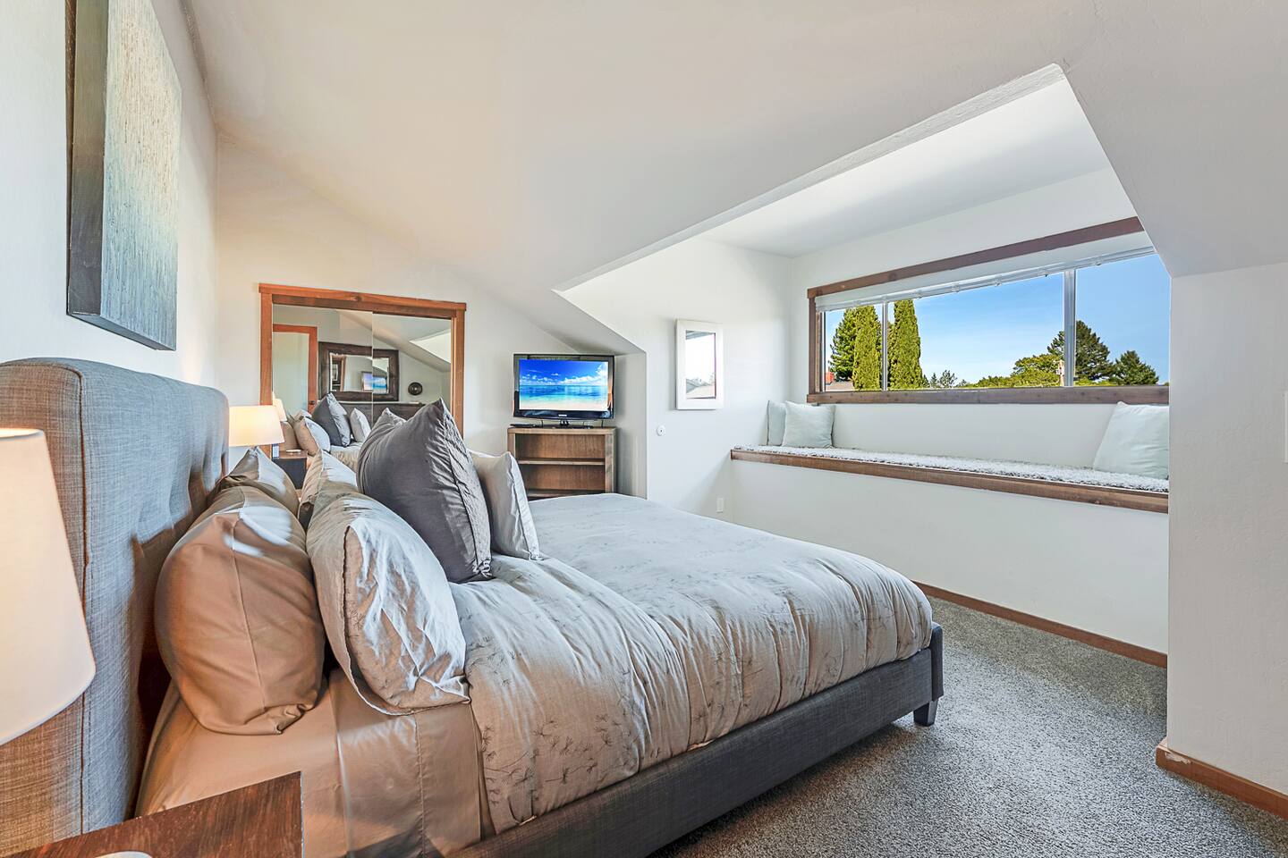 Unwind in the spacious upstairs king bedroom, featuring a cozy window seat with stunning views. Relax and enjoy reading a book from the comfort of your bed, soaking in the serene panorama.