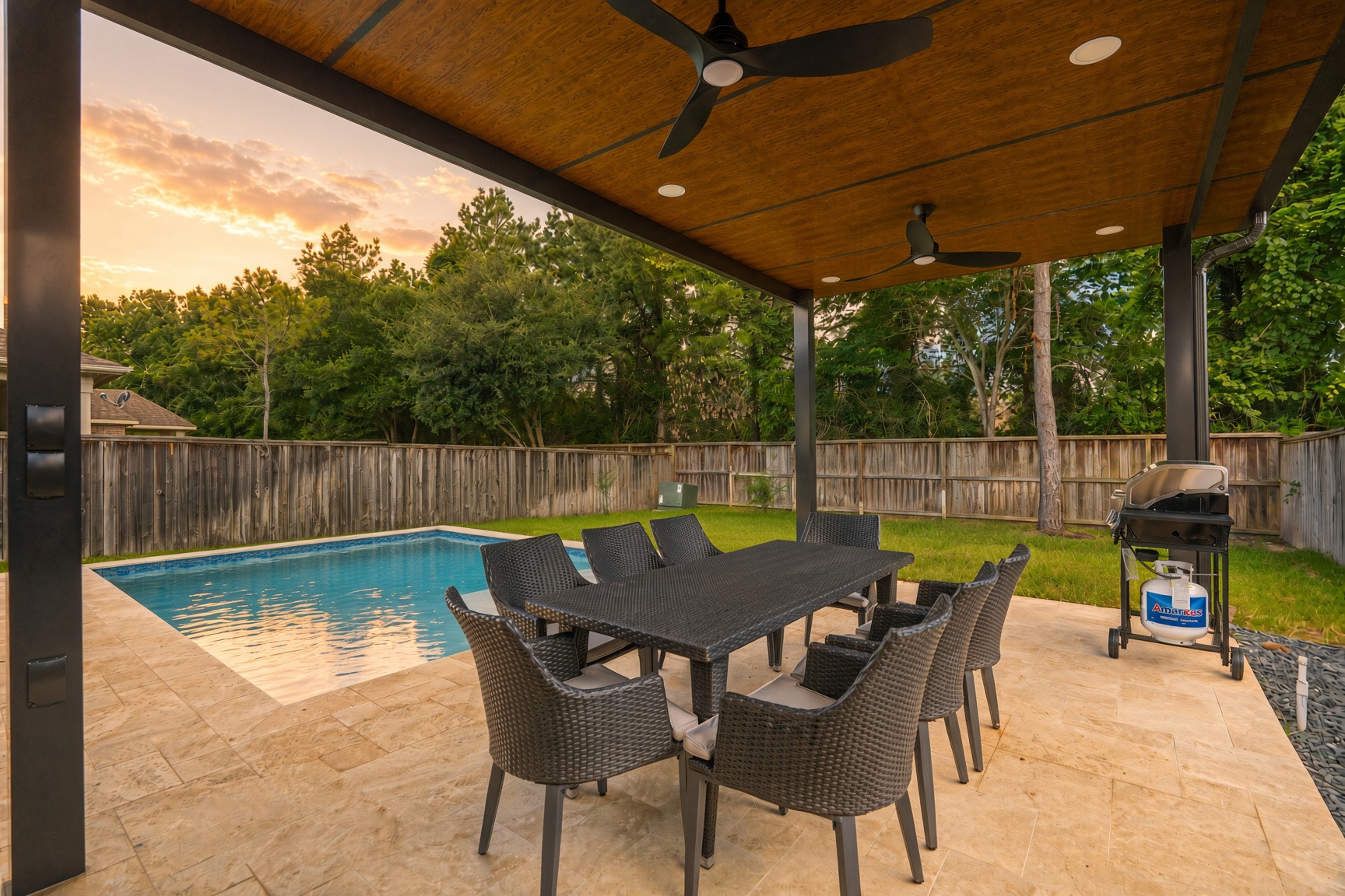 Covered poolside patio with outdoor dining, grill, and serene backyard views