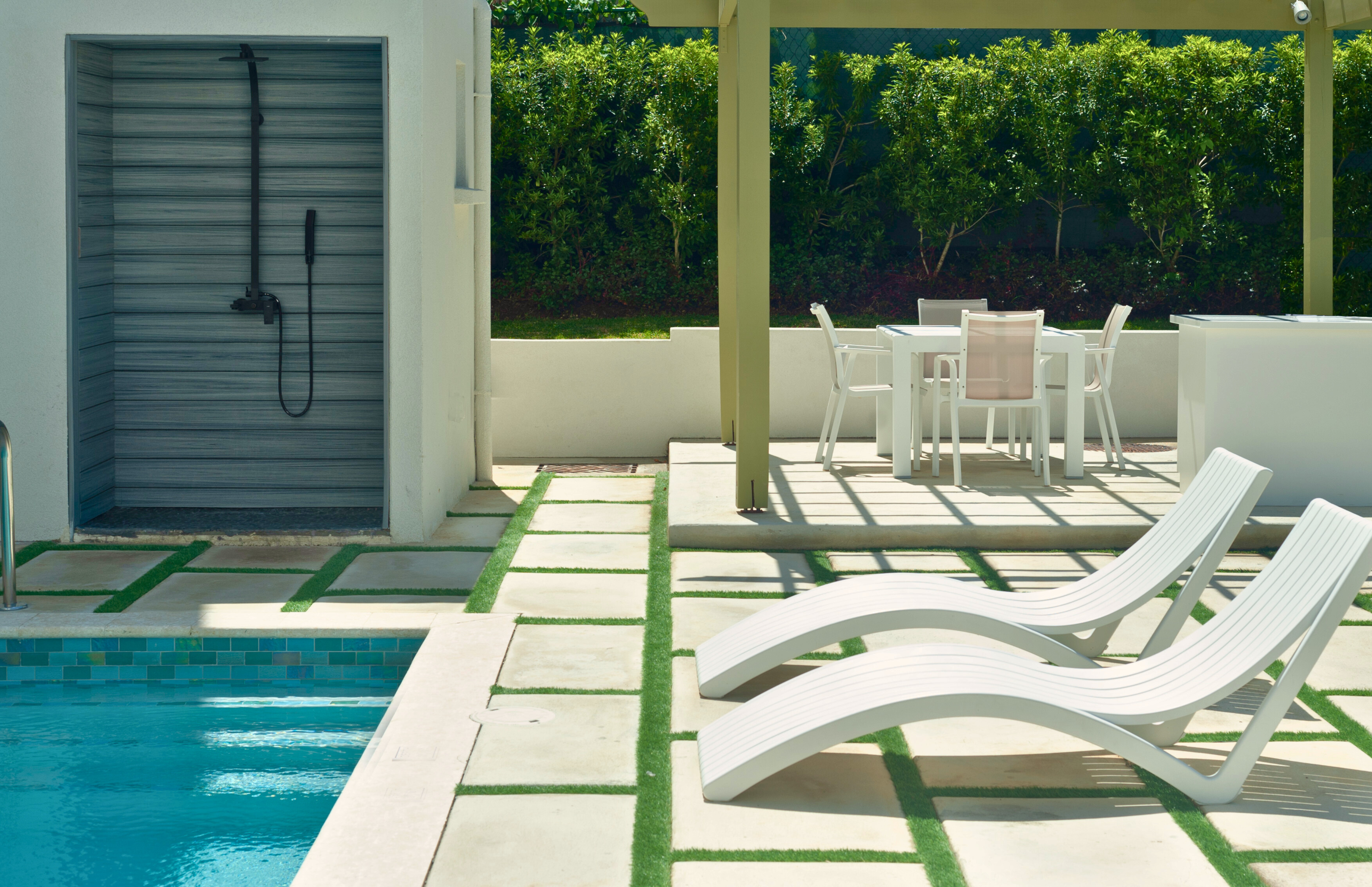 Modern pool patio with loungers, outdoor dining, and private shower
