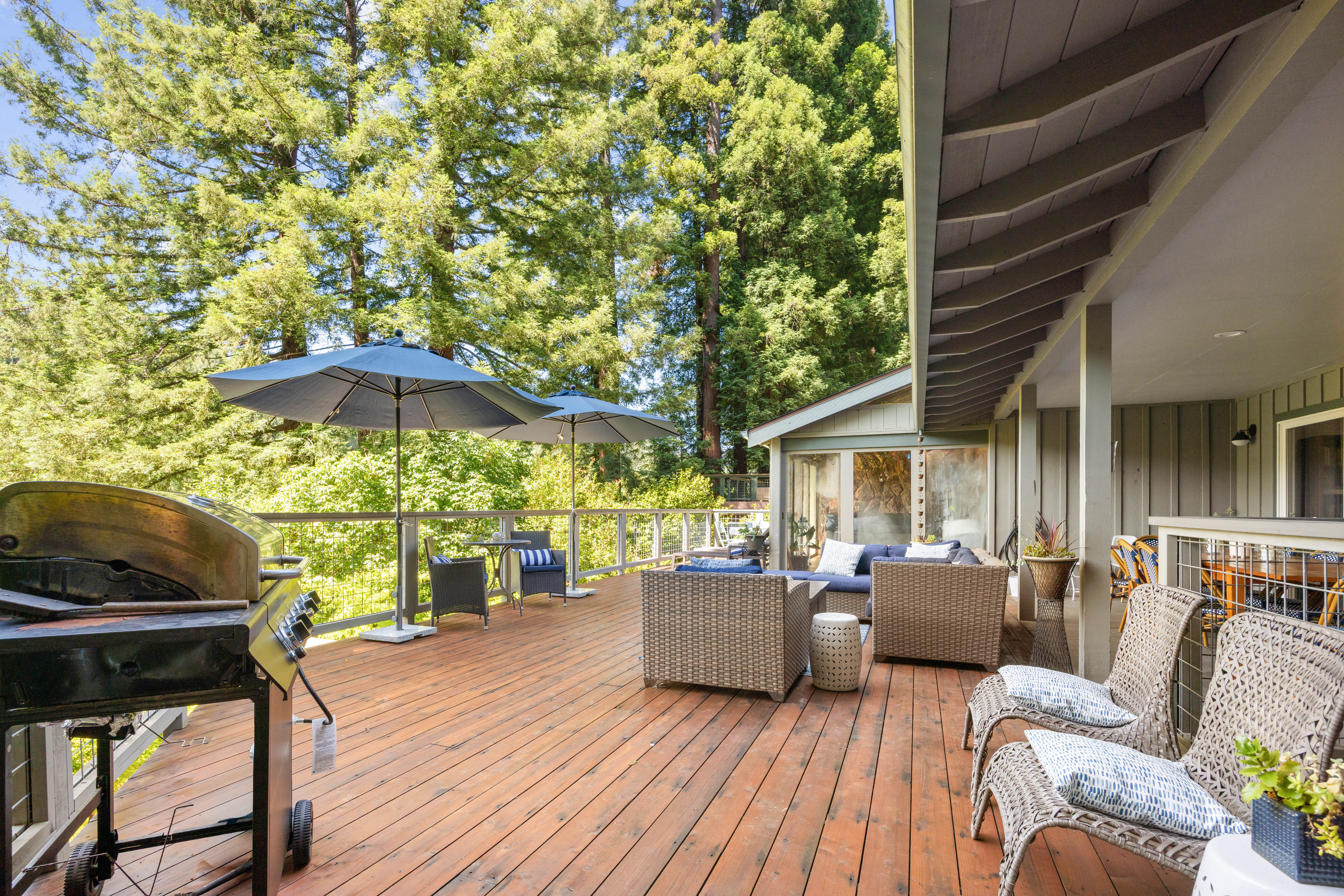 Spacious forest-view deck with lounge seating, umbrellas, and grill