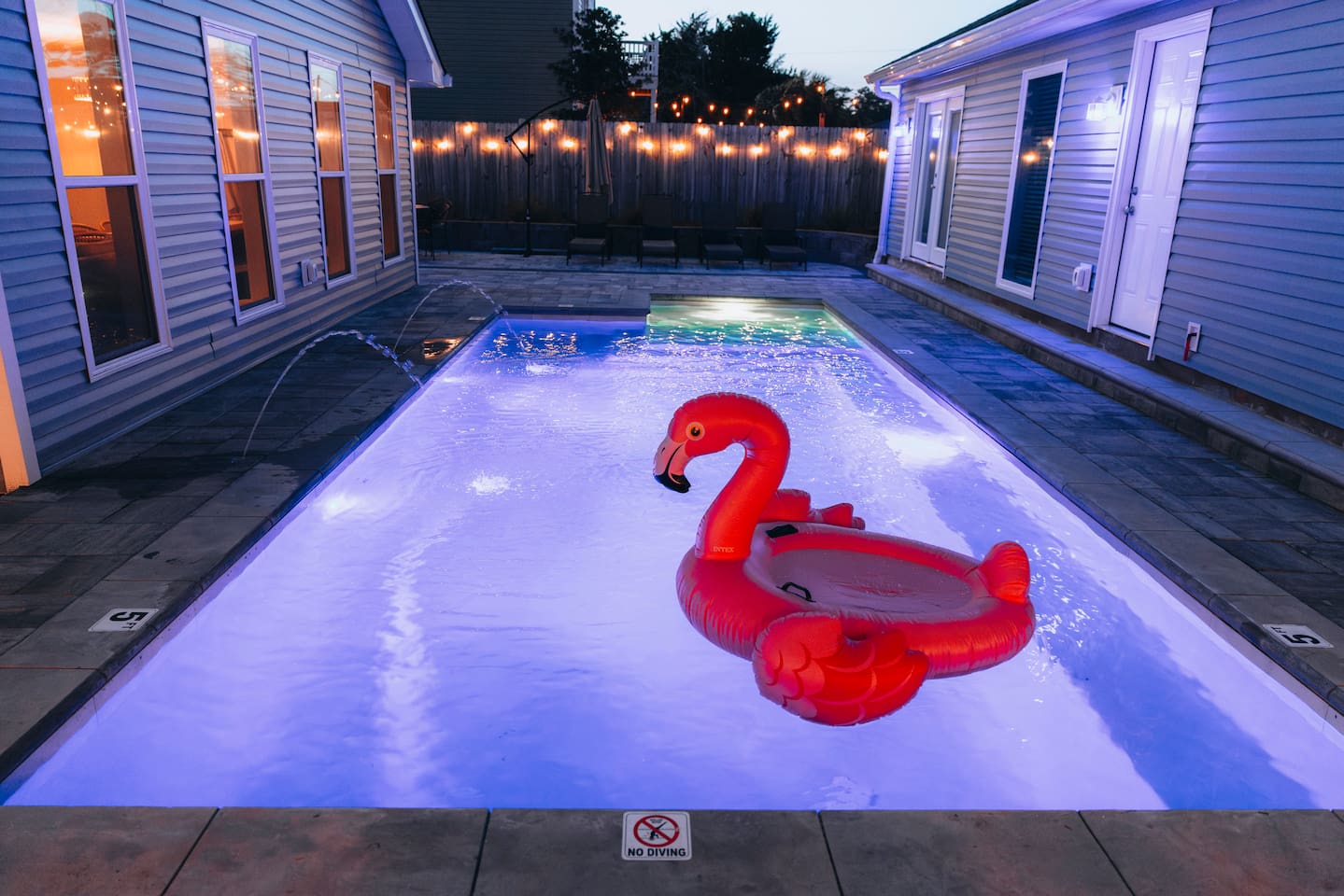 Paver deck and string lights around the illuminated pool at twilight