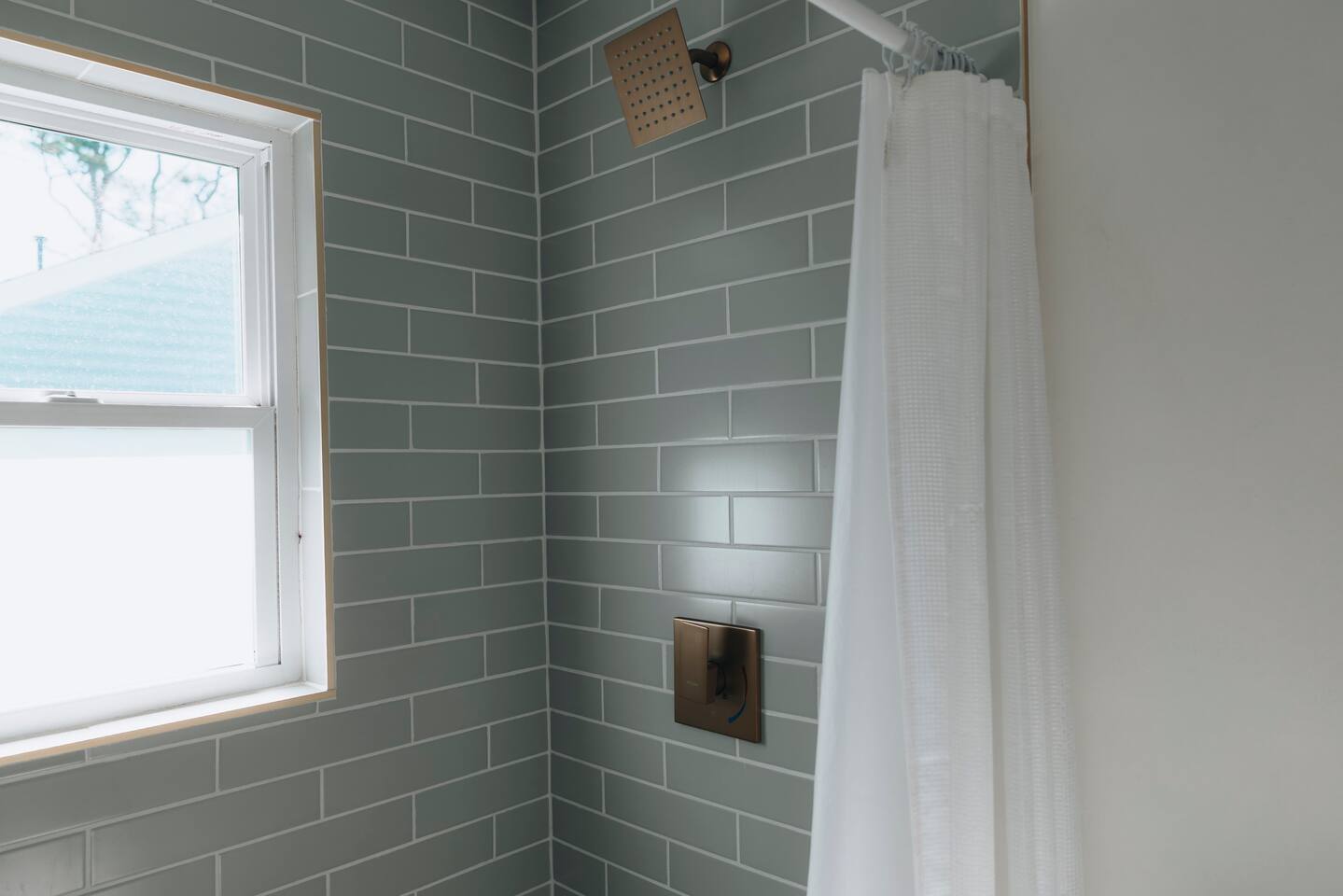 Square rain shower head set against green subway tile