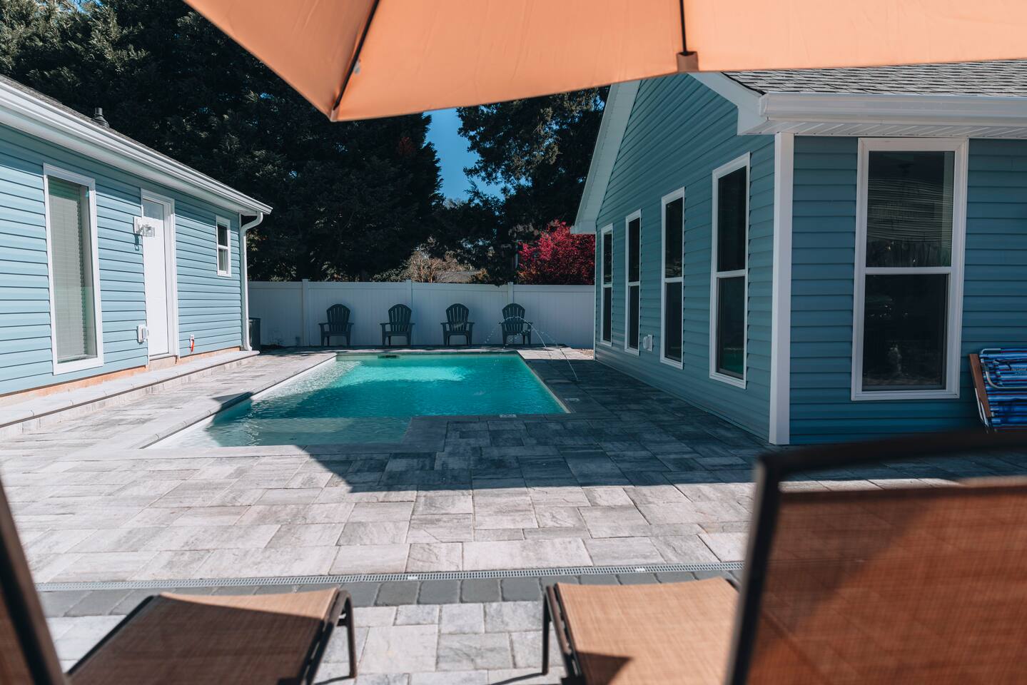 Paved pool deck with lounge chairs set under an orange umbrella