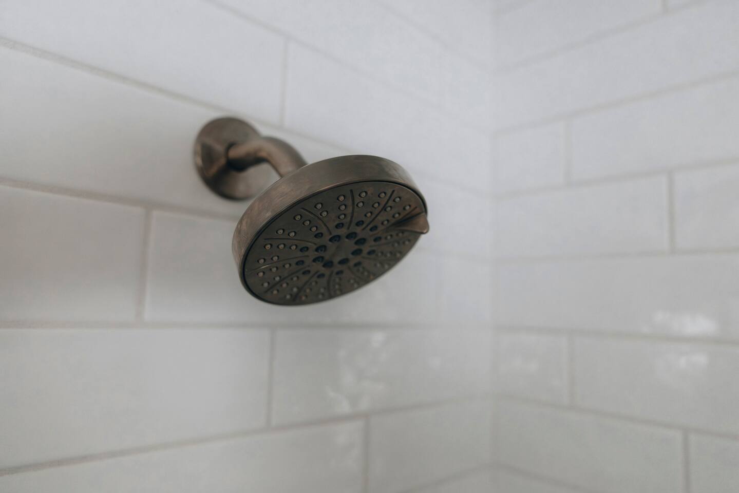 Bronze shower head against white tile