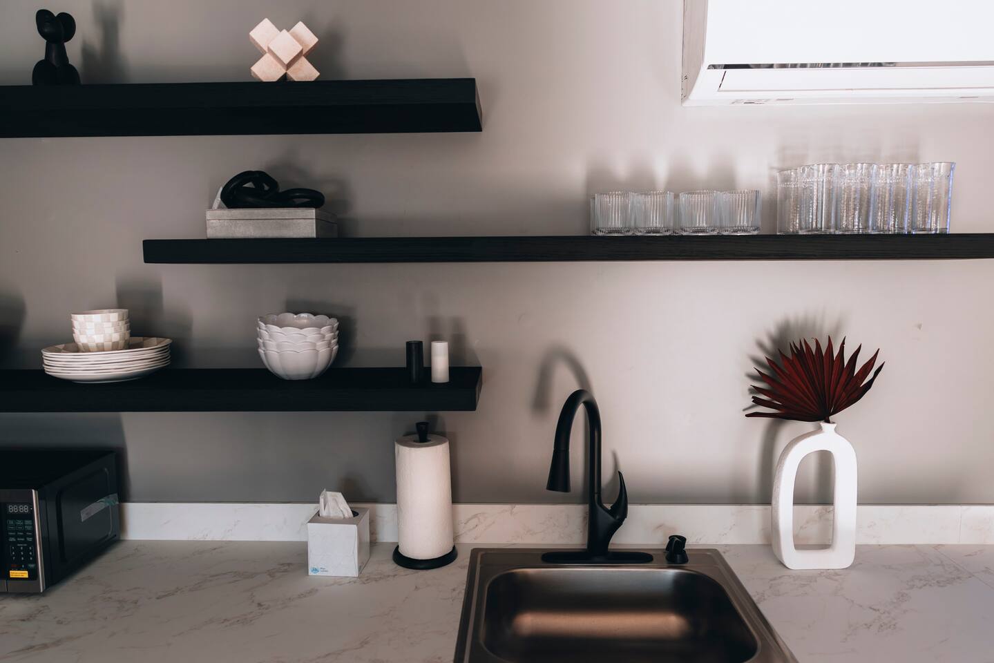 Black open shelving above the kitchen sink, stocked with glasses and bowls