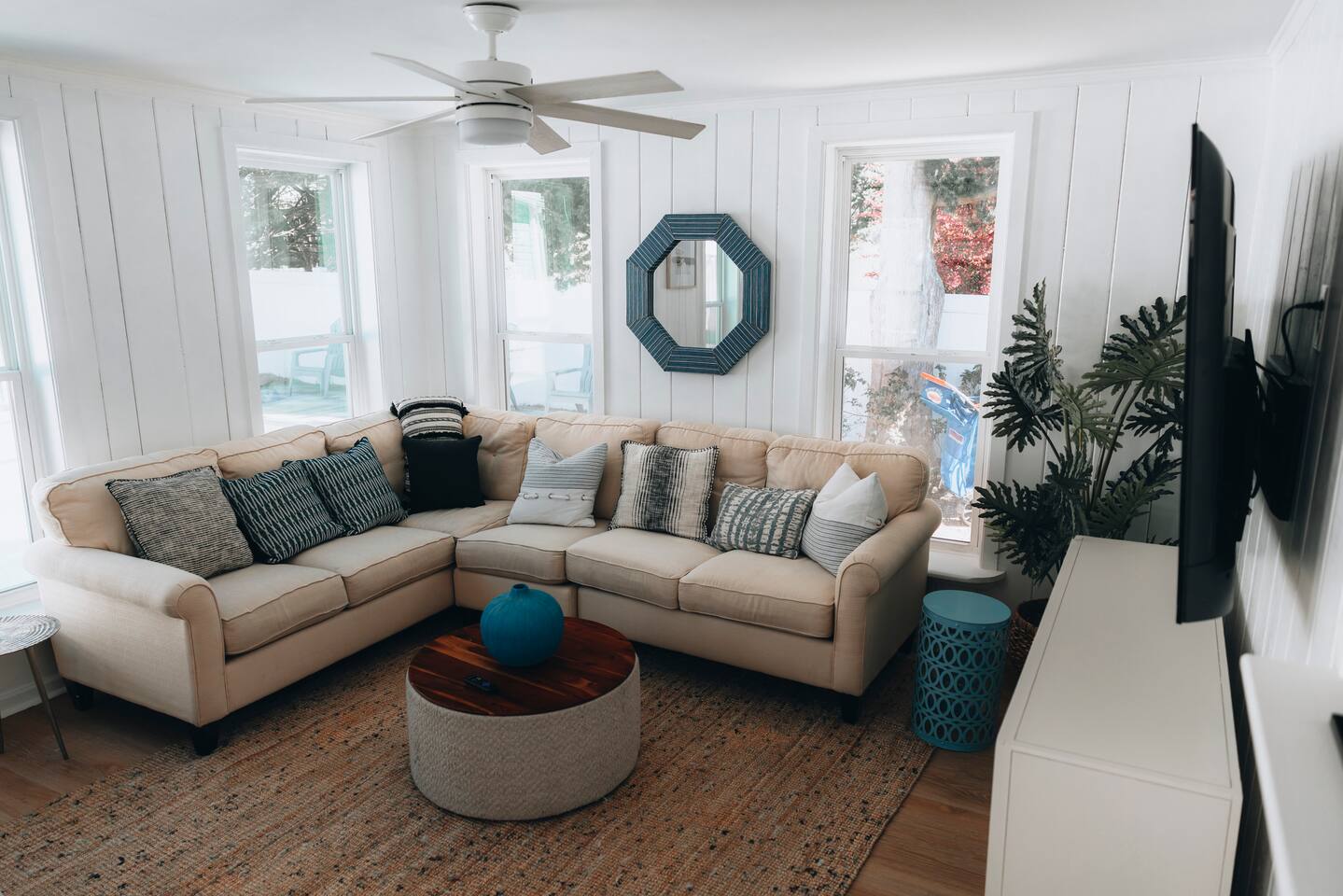 Sectional sofa, wall-mounted TV and ceiling fan in the white-panelled living room