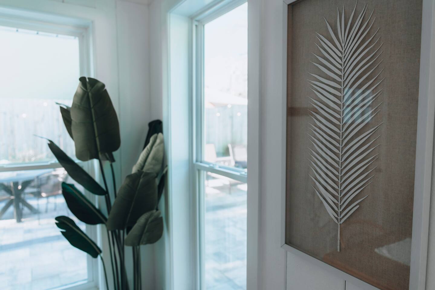 Framed palm frond print beside windows looking out to the patio