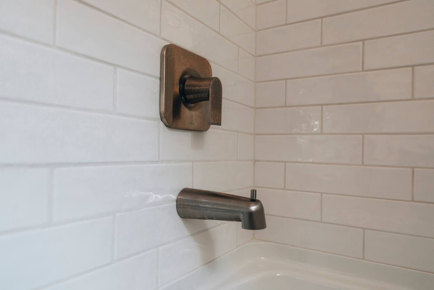 Bronze tub spout and single-handle valve on white tile
