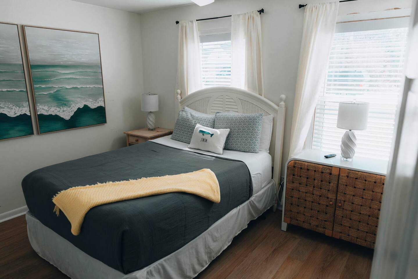 Queen bed between two windows, woven nightstand alongside
