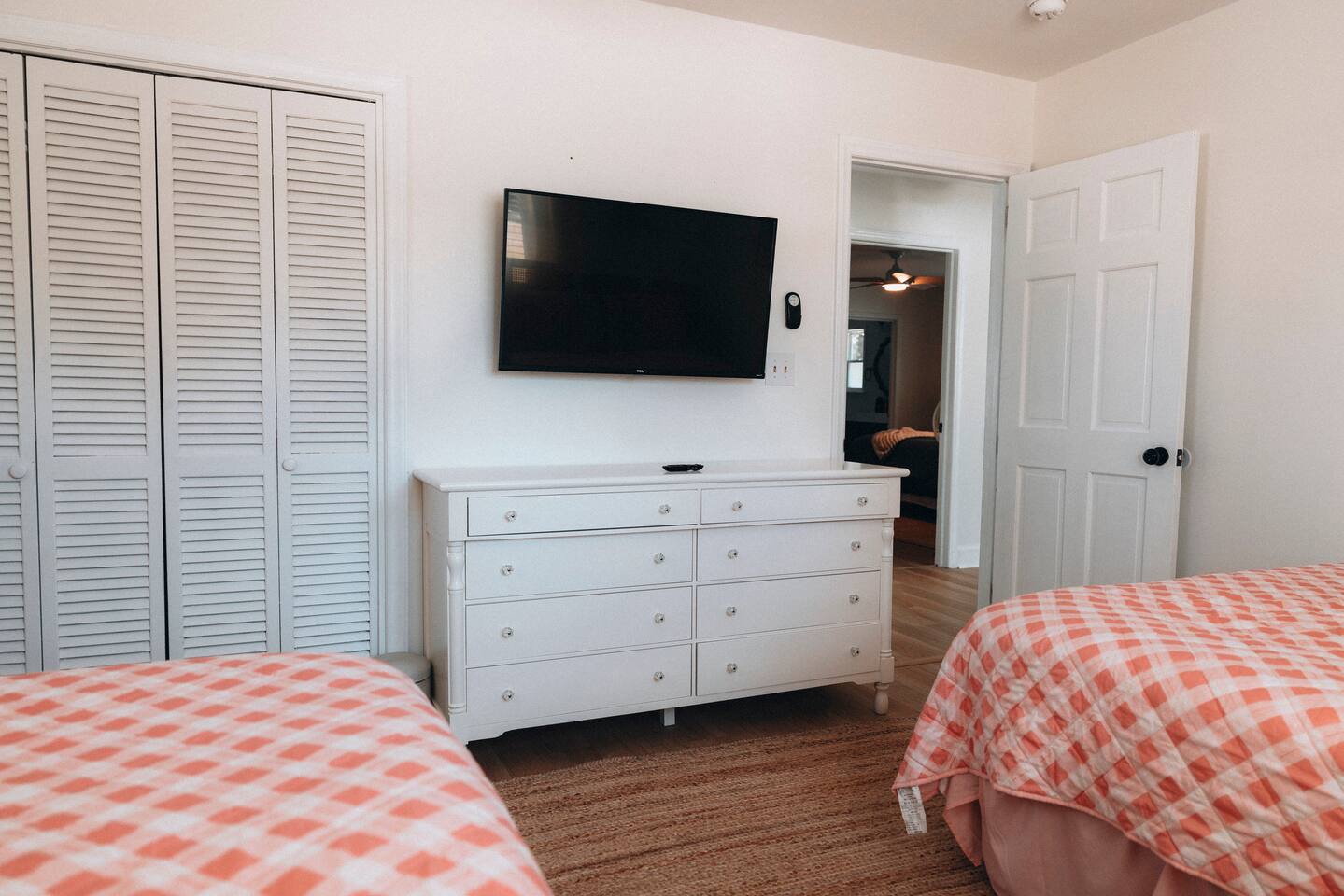 Same bedroom's wall-mounted TV, dresser and louvred closet doors