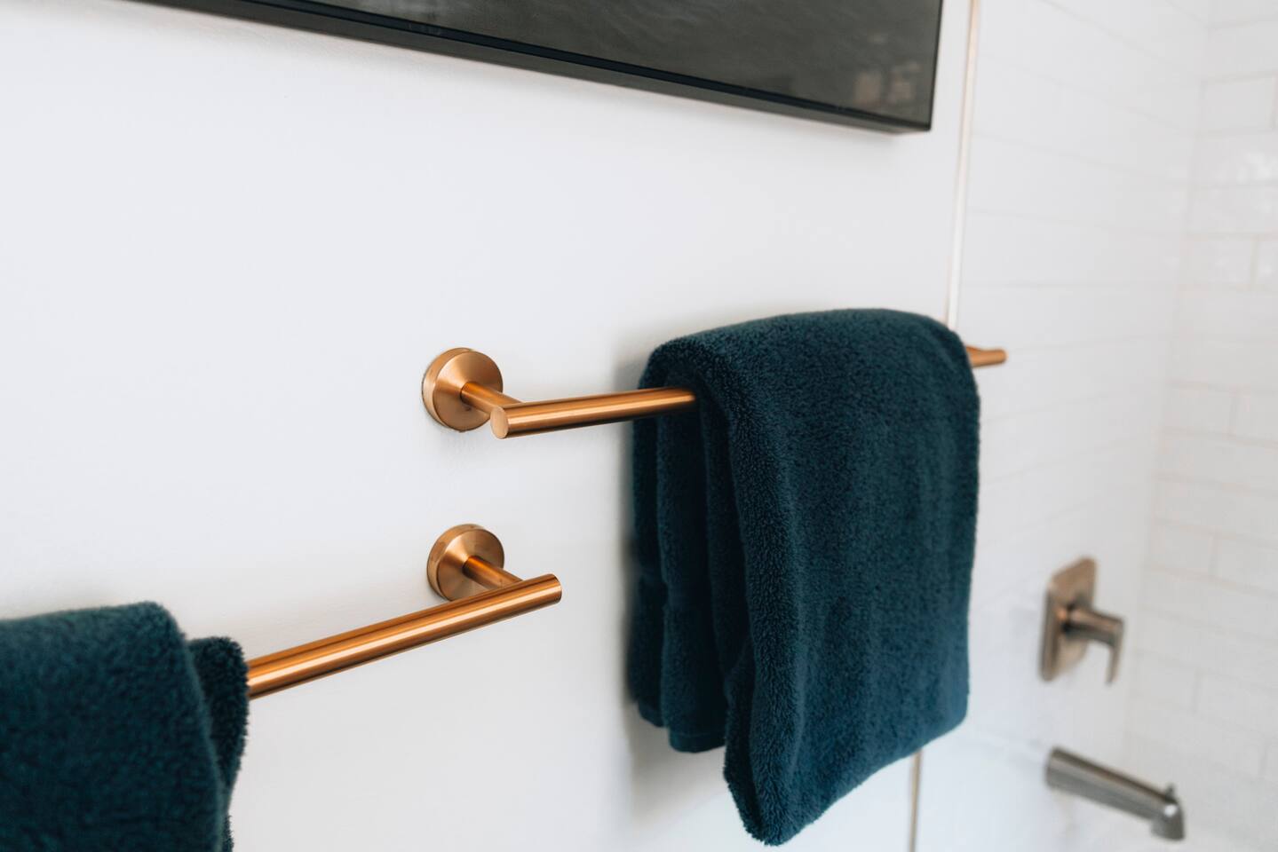 Brushed brass towel bars holding folded teal towels