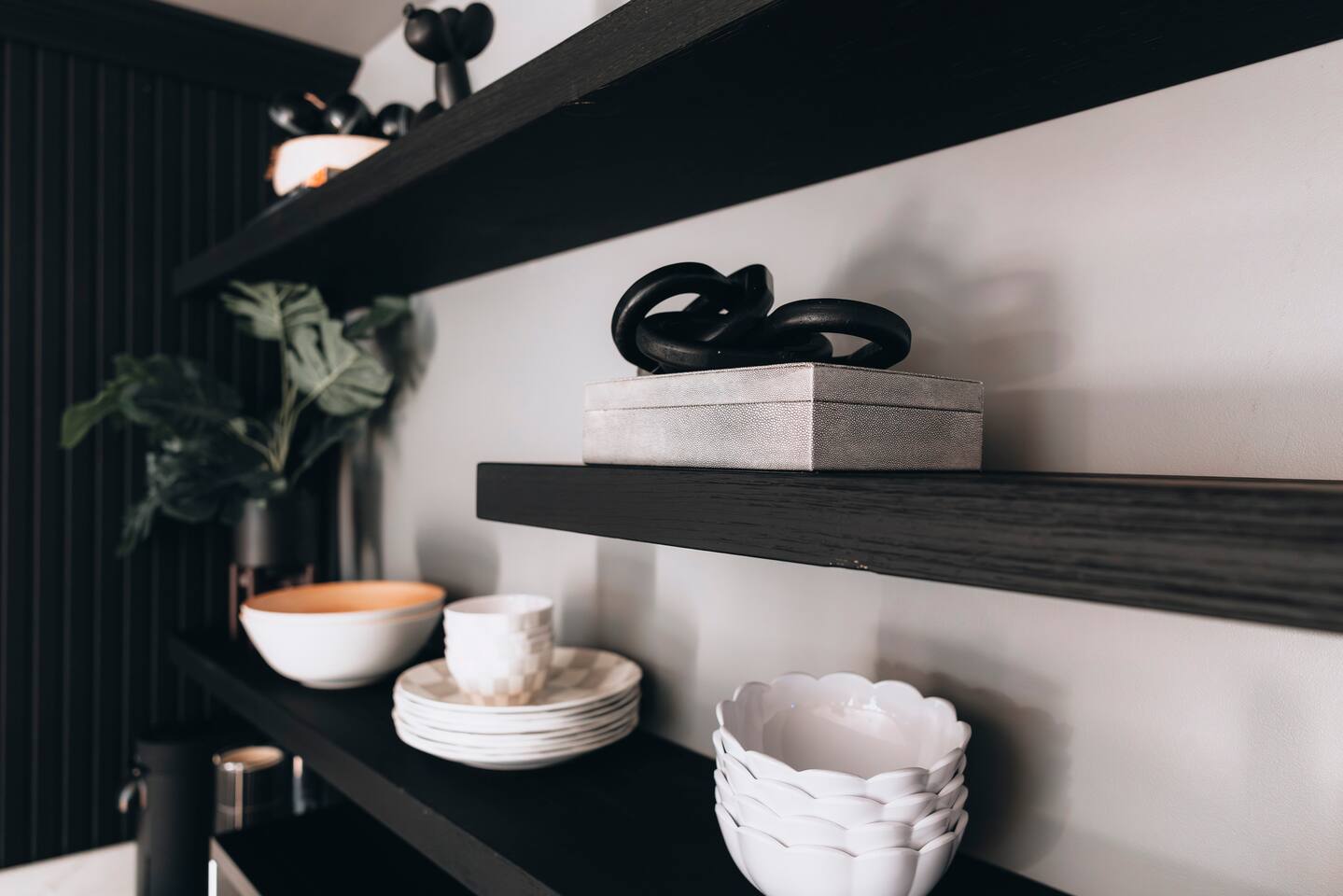Black floating shelves holding white bowls, plates and a decorative box