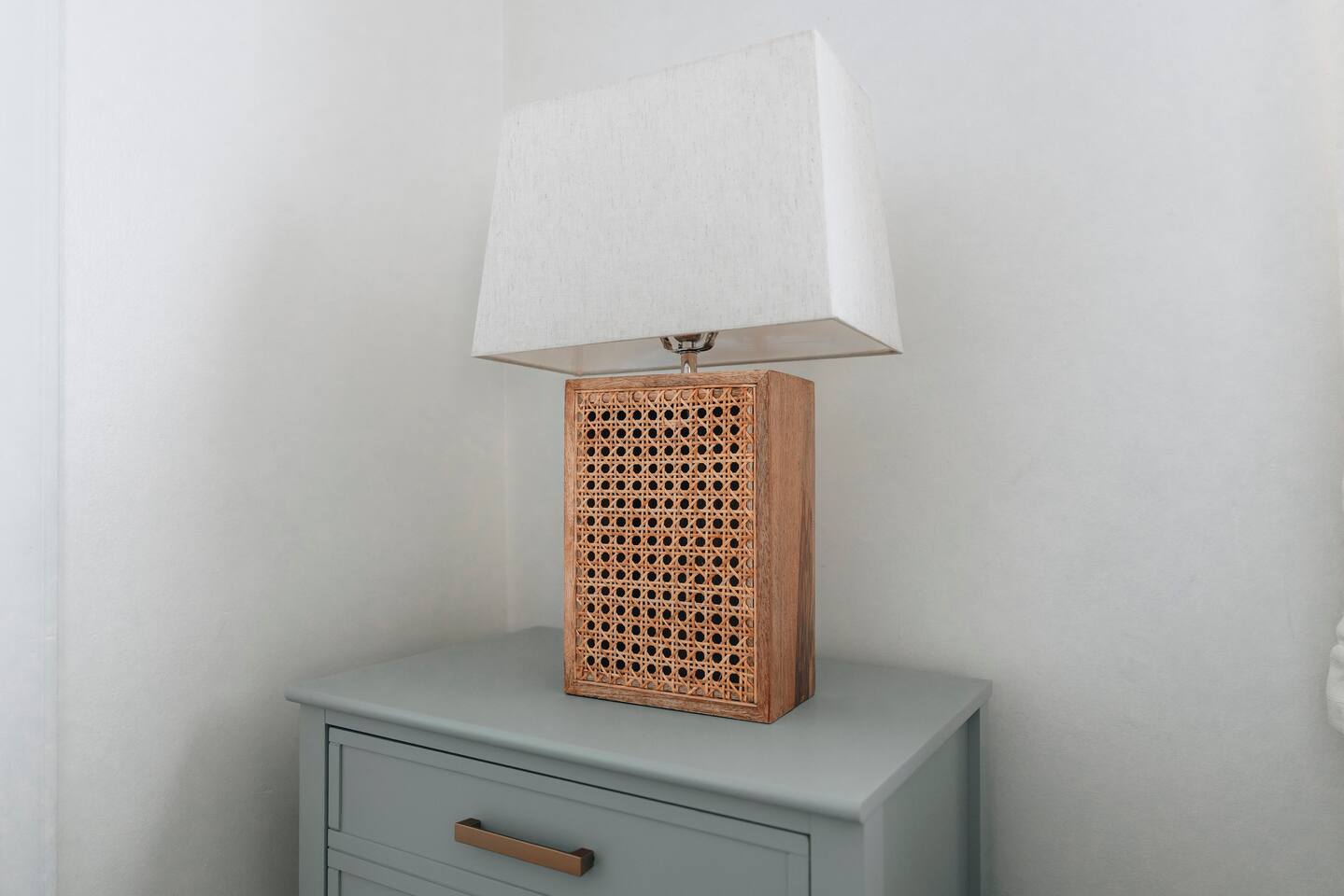 Caned table lamp with a linen shade on a sage nightstand