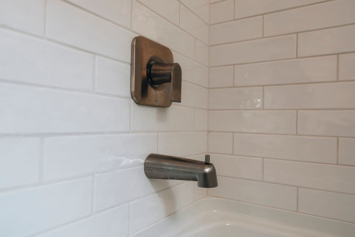 Bronze tub spout and mixer set into white tile