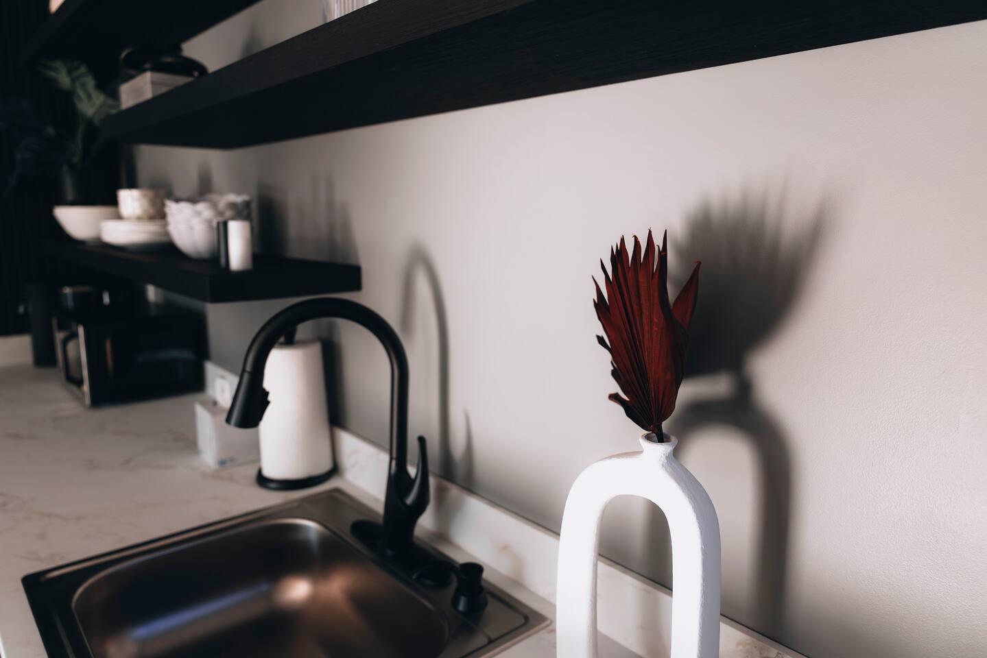 Wet bar sink with black faucet and a white vase