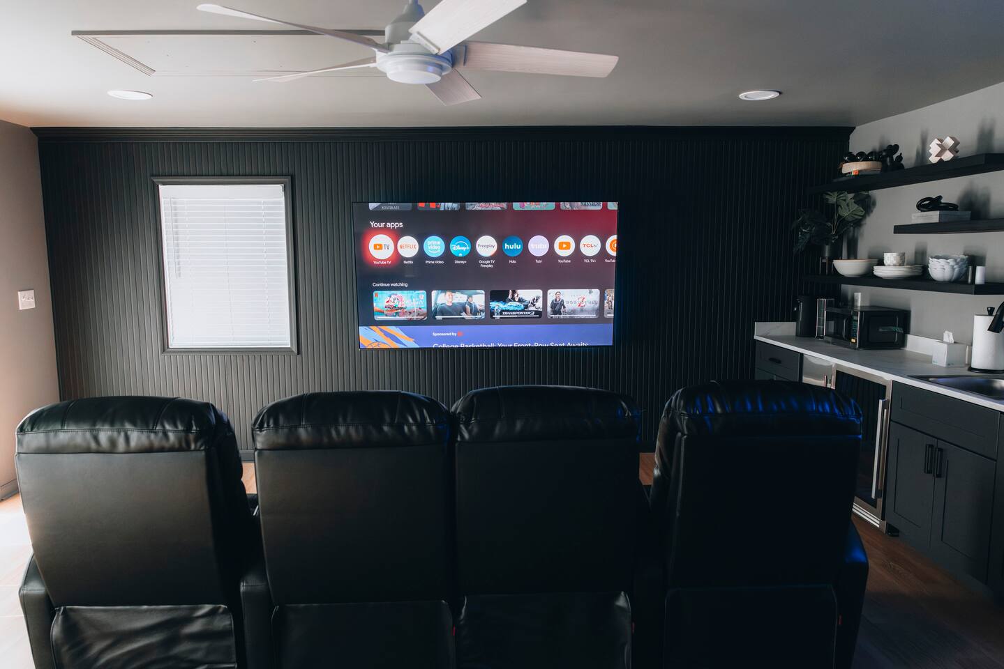 Media room with four black recliners facing a wall-mounted smart TV