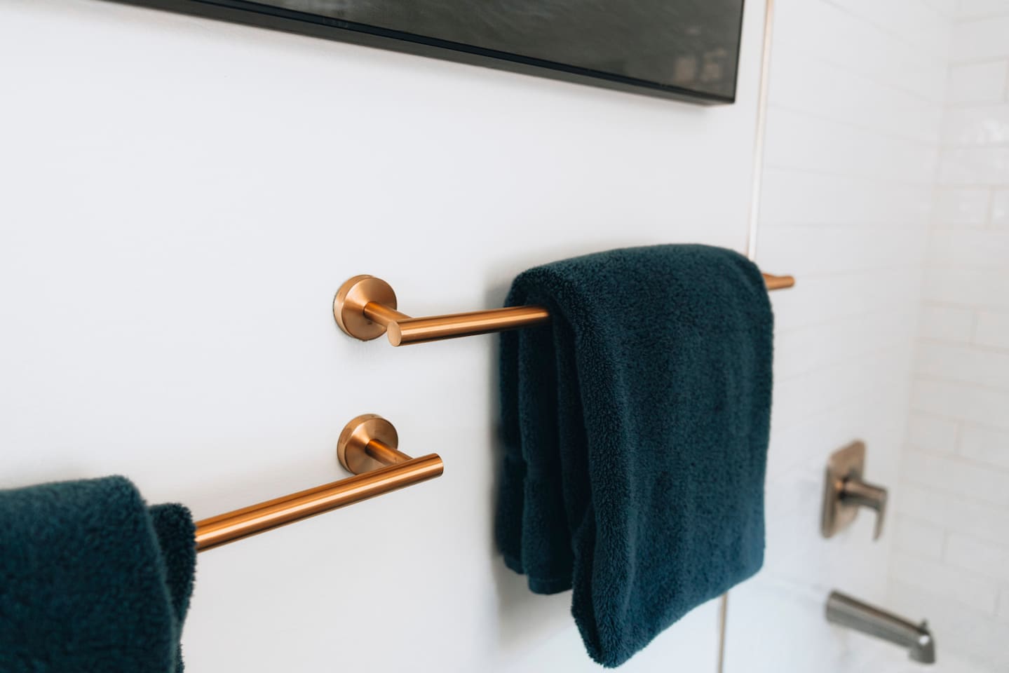 Teal towels on brushed copper bars beside the tiled shower