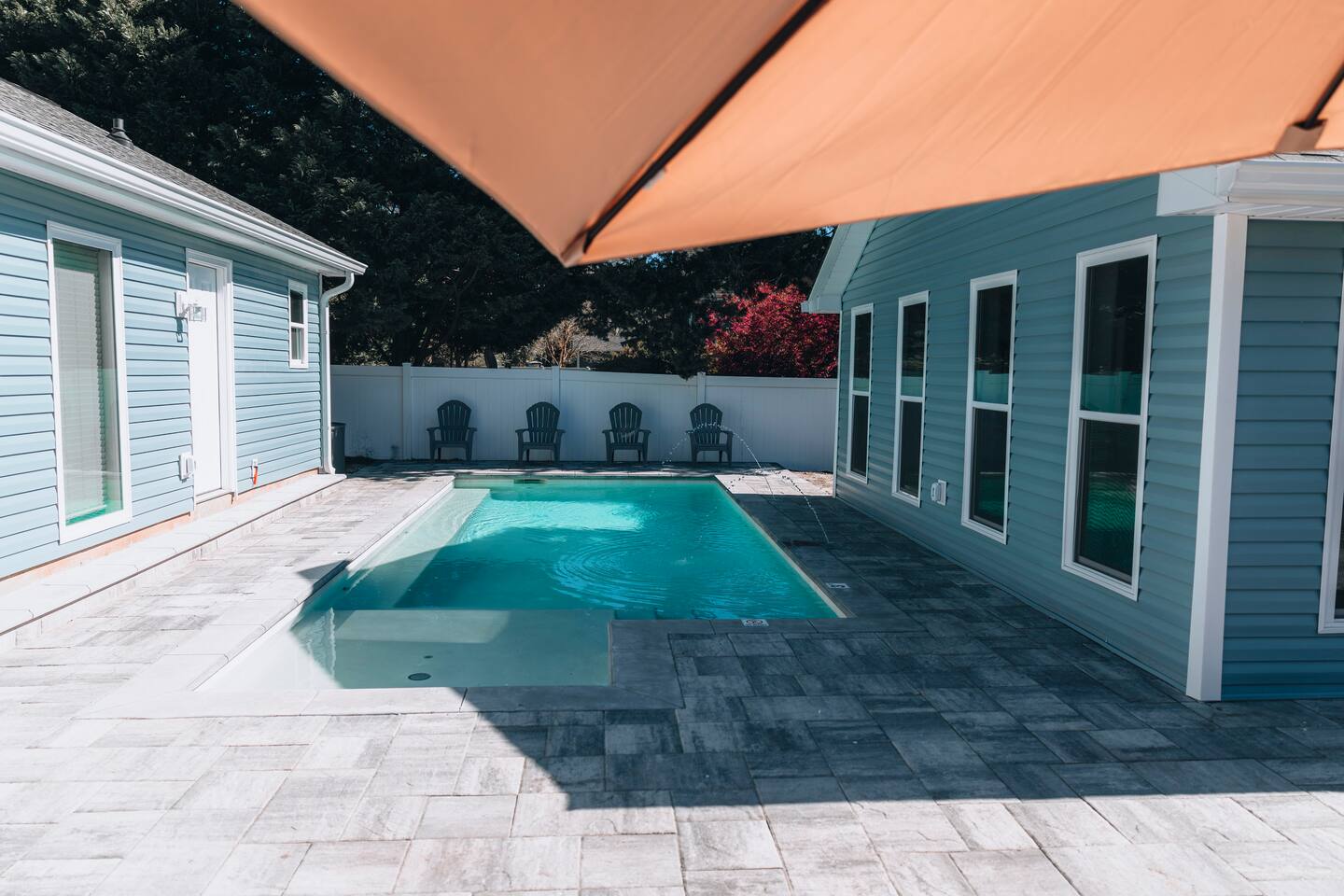 The pool from beneath the shade umbrella, with Adirondack chairs along the fence