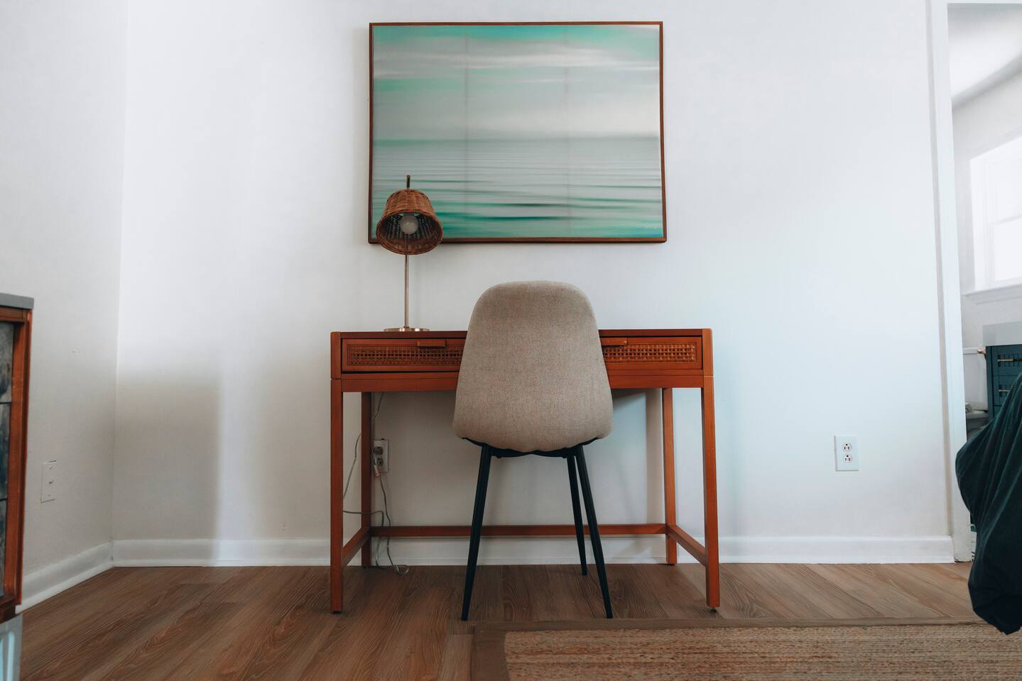 Wooden desk and chair under a framed seascape print