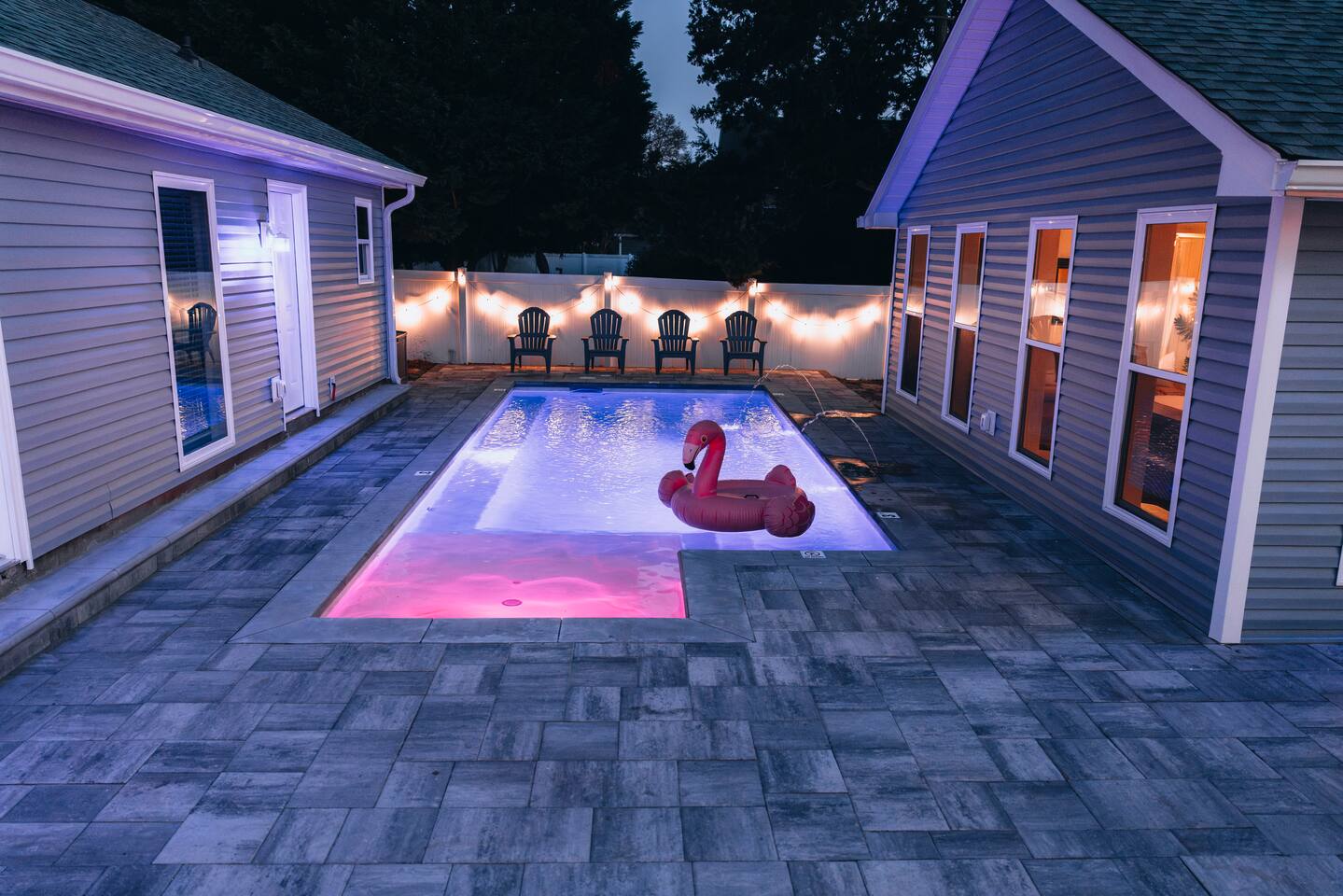 The pool lit blue and pink at dusk, string lights along the fence