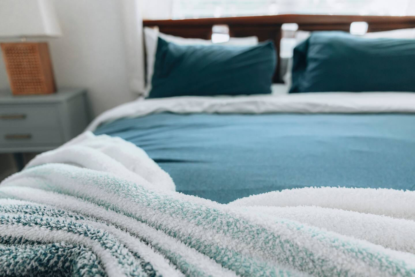 Teal bedding and a soft striped throw on a wood-framed bed