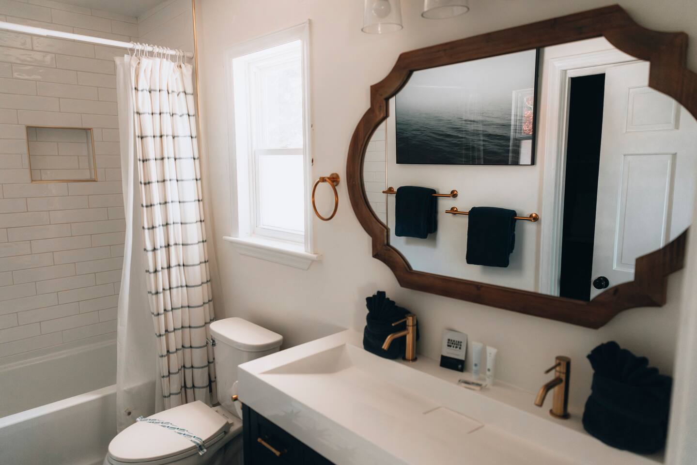 Bathroom with tub and shower, arched wood mirror and brass fixtures