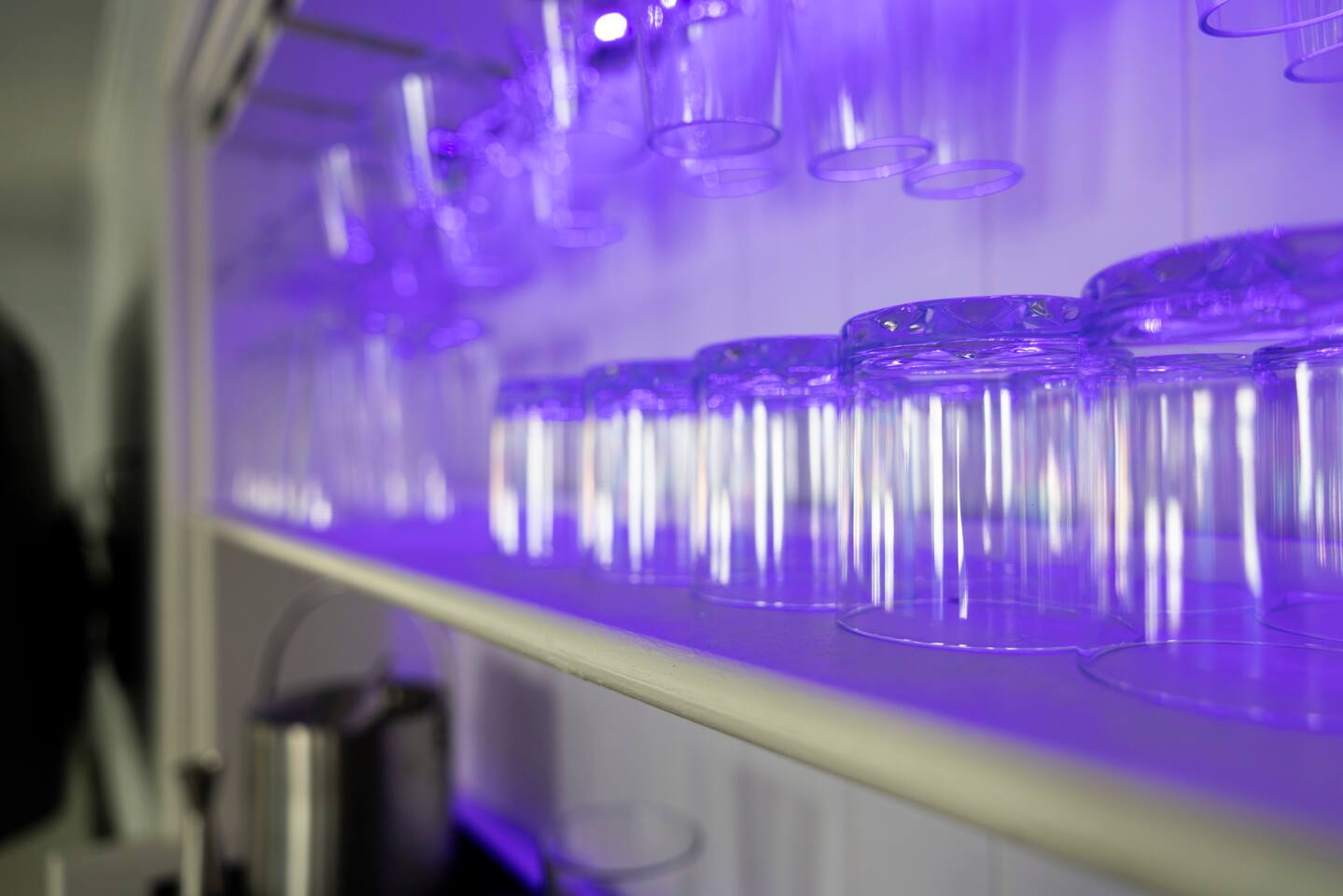 Glassware lined up on a shelf under violet accent lighting