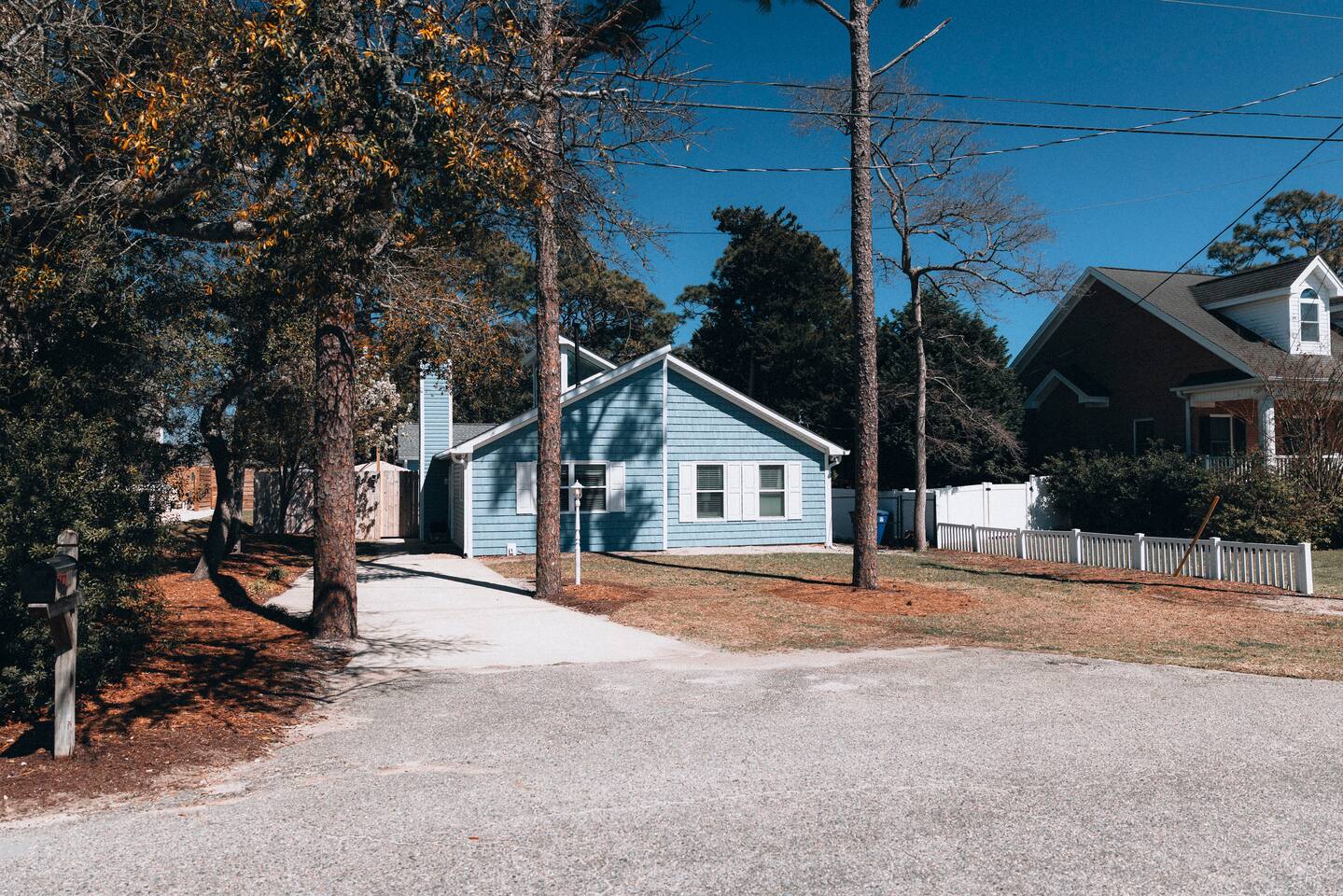 The blue cottage from the street, with driveway parking under pines