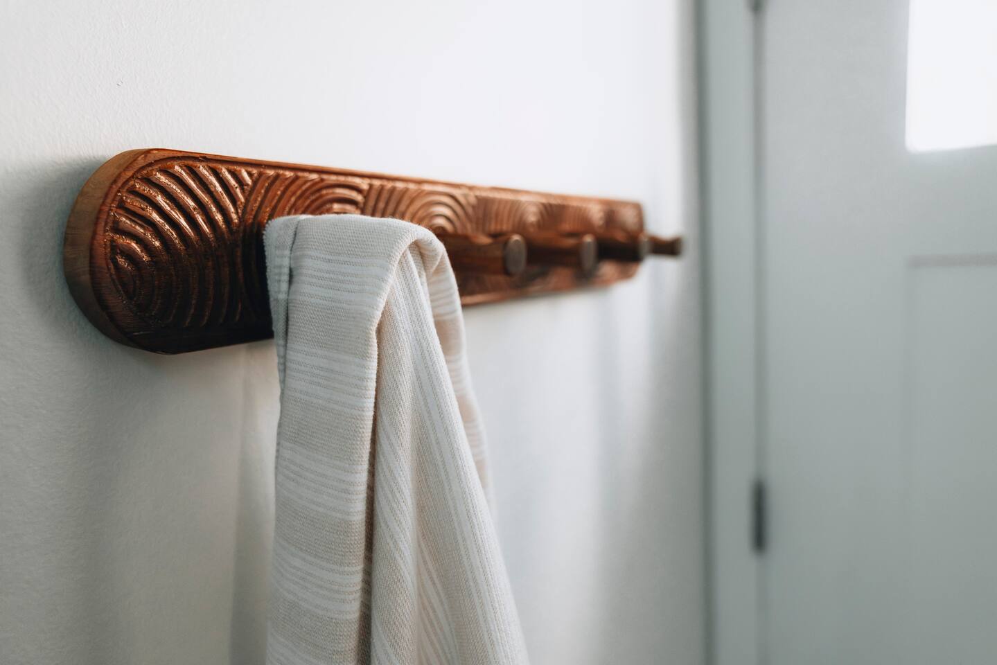 Carved wooden peg rail holding a striped hand towel