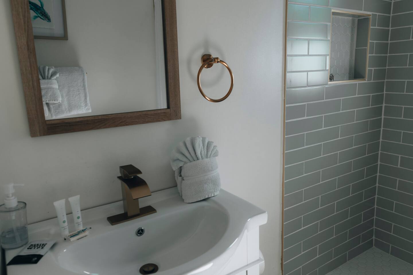 Bathroom vanity with brushed bronze fixtures beside a green-tiled walk-in shower