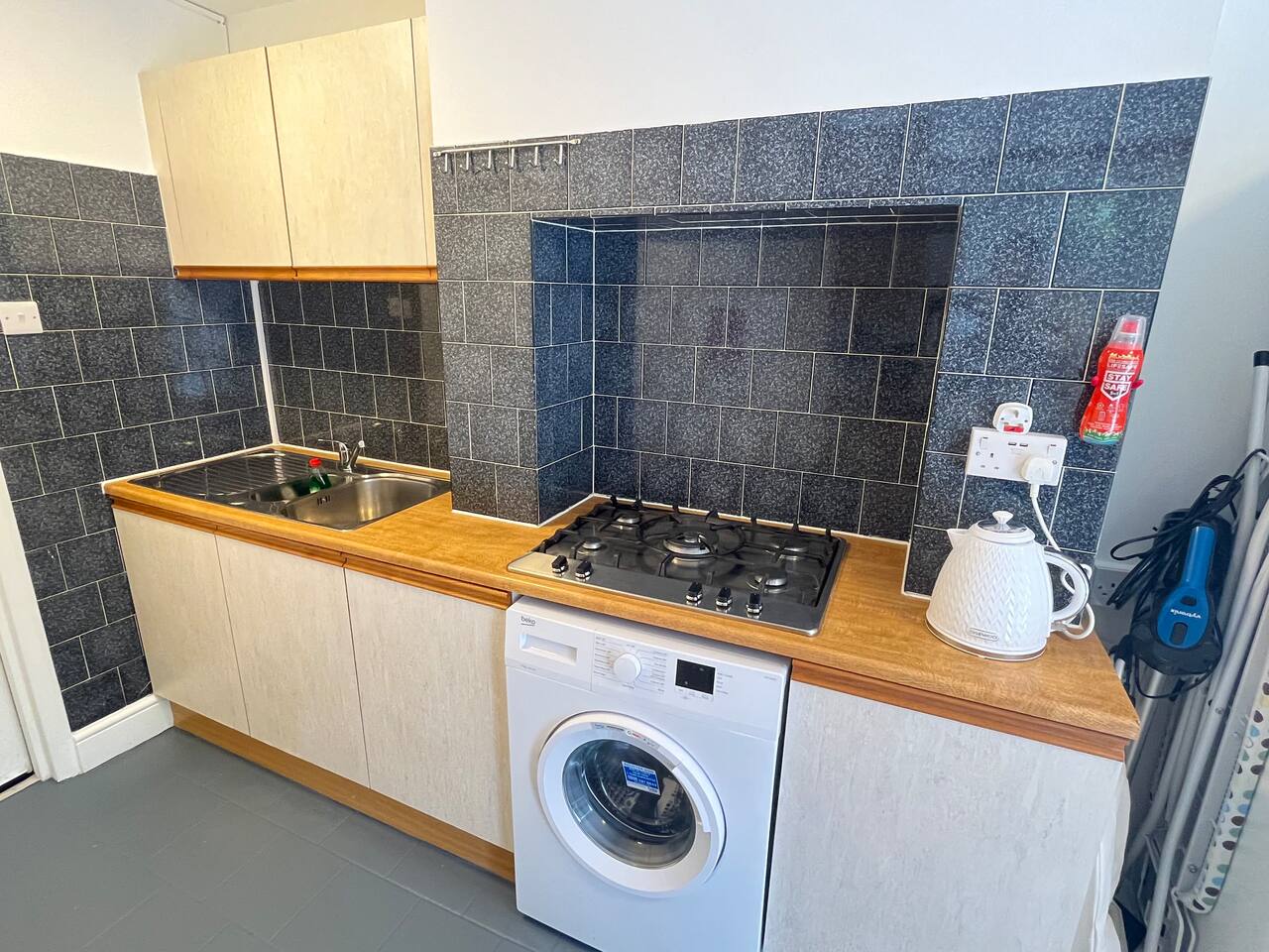 Simple kitchen in Shepherd’s Bush with gas cooktop, washer and sleek black tile backsplash. A practical setup just minutes from Hammersmith in West London’s vibrant heart.