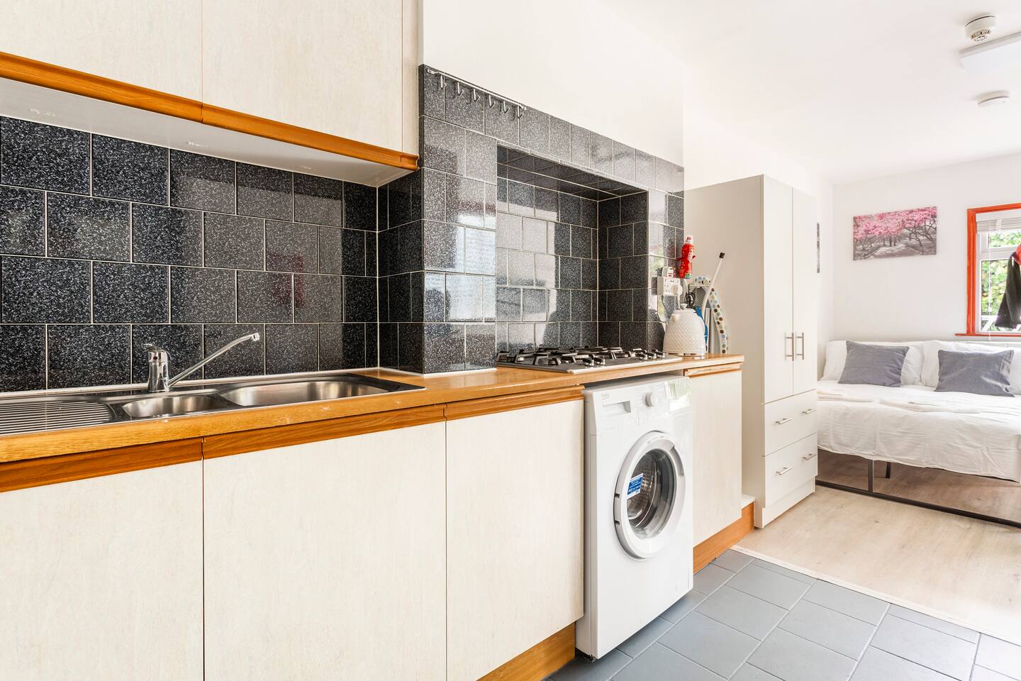 Simple kitchen in Shephard's Bush, Greater London featuring a gas cooktop, washer, and sleek black tile backsplash.