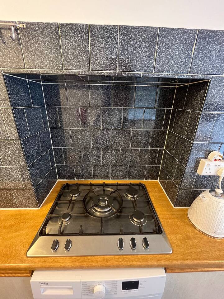 Bright kitchen with black tile design, a gas stove, white washer, and electric kettle.