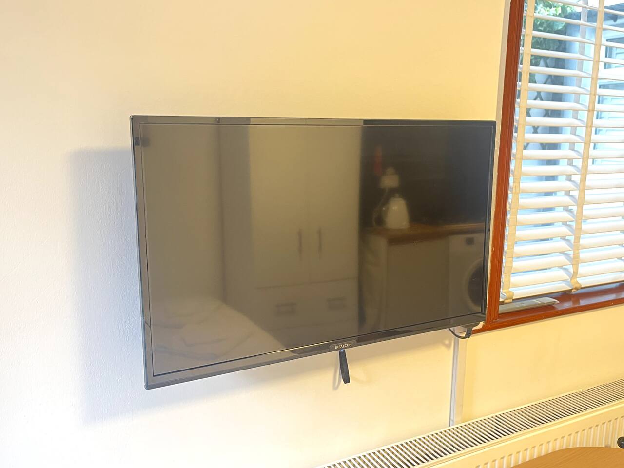 Wall-mounted Finlux TV with blinds, radiator, and soft room lighting.